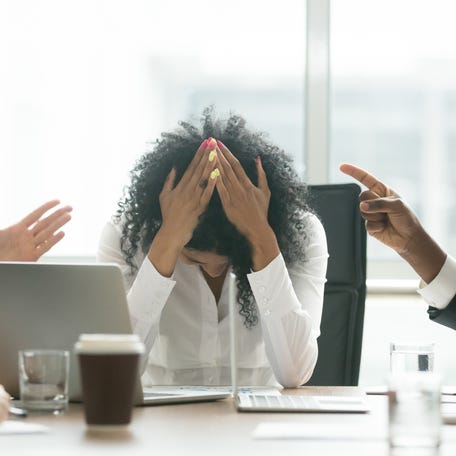 Upset depressed black woman leader suffering from gender discrimination inequality at work, diverse men colleagues pointing fingers scolding bullying frustrated african businesswoman at workplace