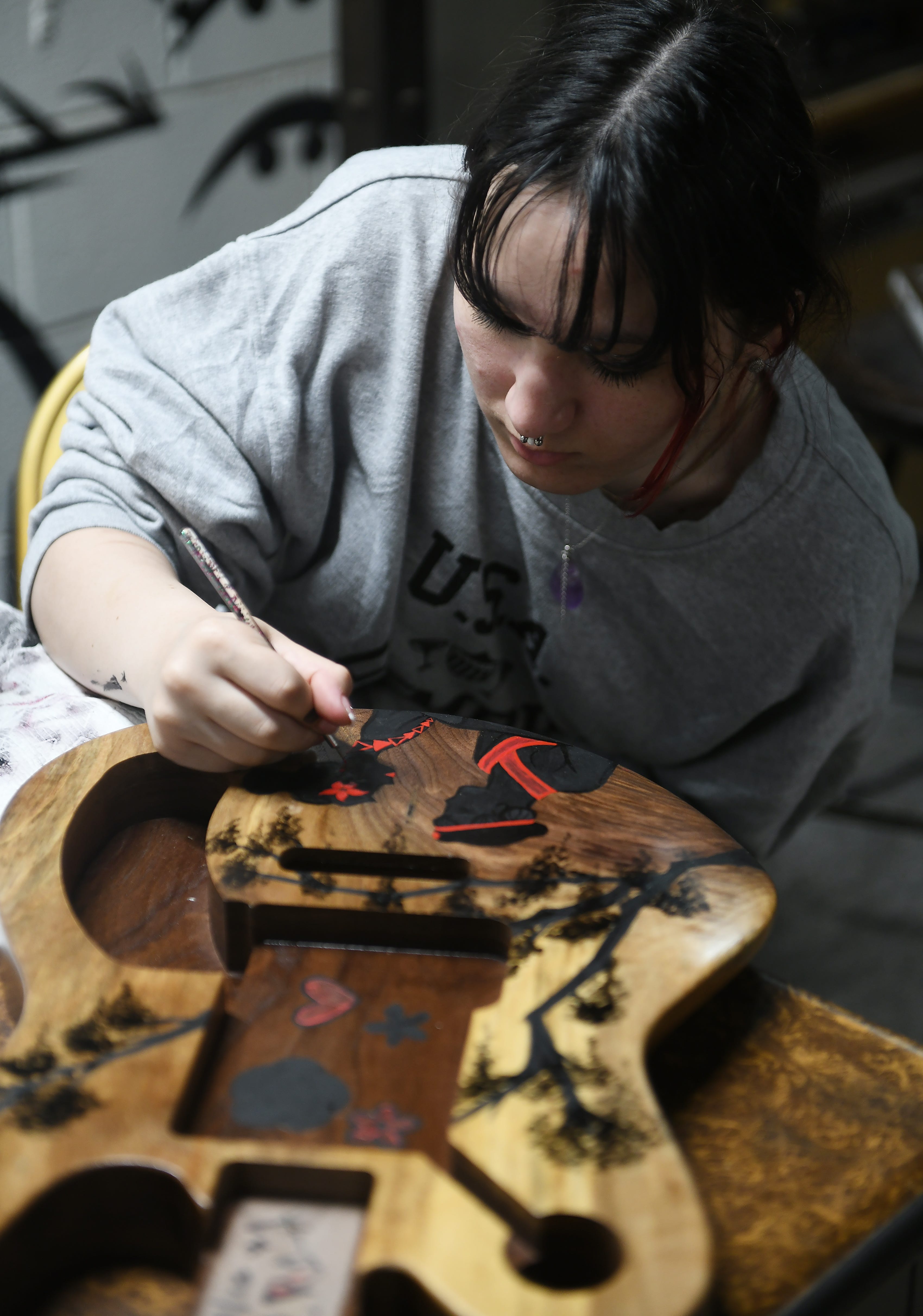 Gabriel Currie's daughter, Petra Currie, 17, of Taylor paints the front of a guitar at Echopark Guitars in Detroit on Aug. 11, 2023.