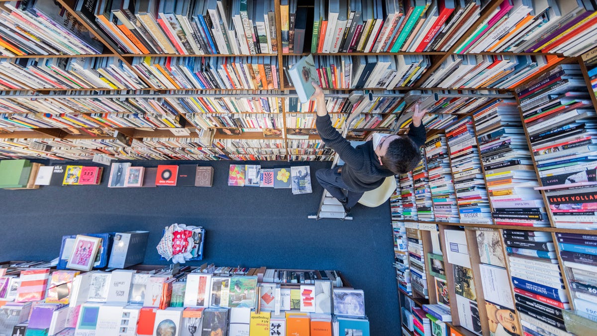 An employee of the Walther Koenig bookshop stands on a ladder in front of a shelf and sorts books in Cologne, Germany, Wednesday, March 3, 2021. The publishing bookshop specialises in art and art science, architecture, arts and crafts, design, fashion, photography, film and art theory as well as exhibition catalogues. (Rolf Vennenbernd/dpa via AP) ORG XMIT: PRO116