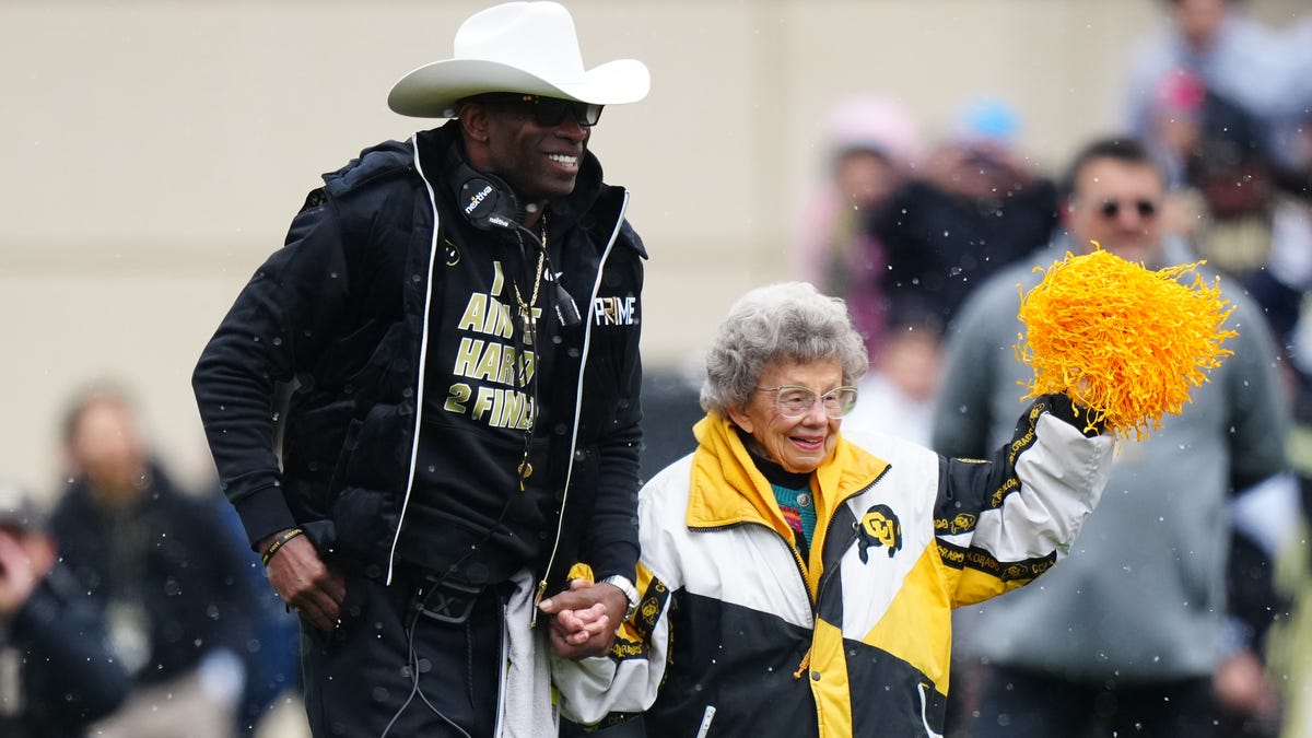 Colorado football coach Deion Sanders walks onto Folsom Field with Peggy Coppom before the start of the spring game in April.