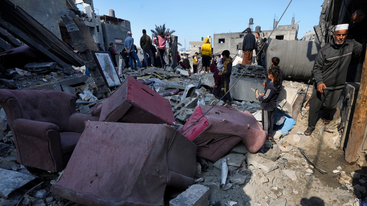 Palestinians look at the destruction of the Al-Gatshan family building after an Israeli strike in Nusseirat refugee camp, central Gaza Strip, Monday, Dec. 18, 2023.