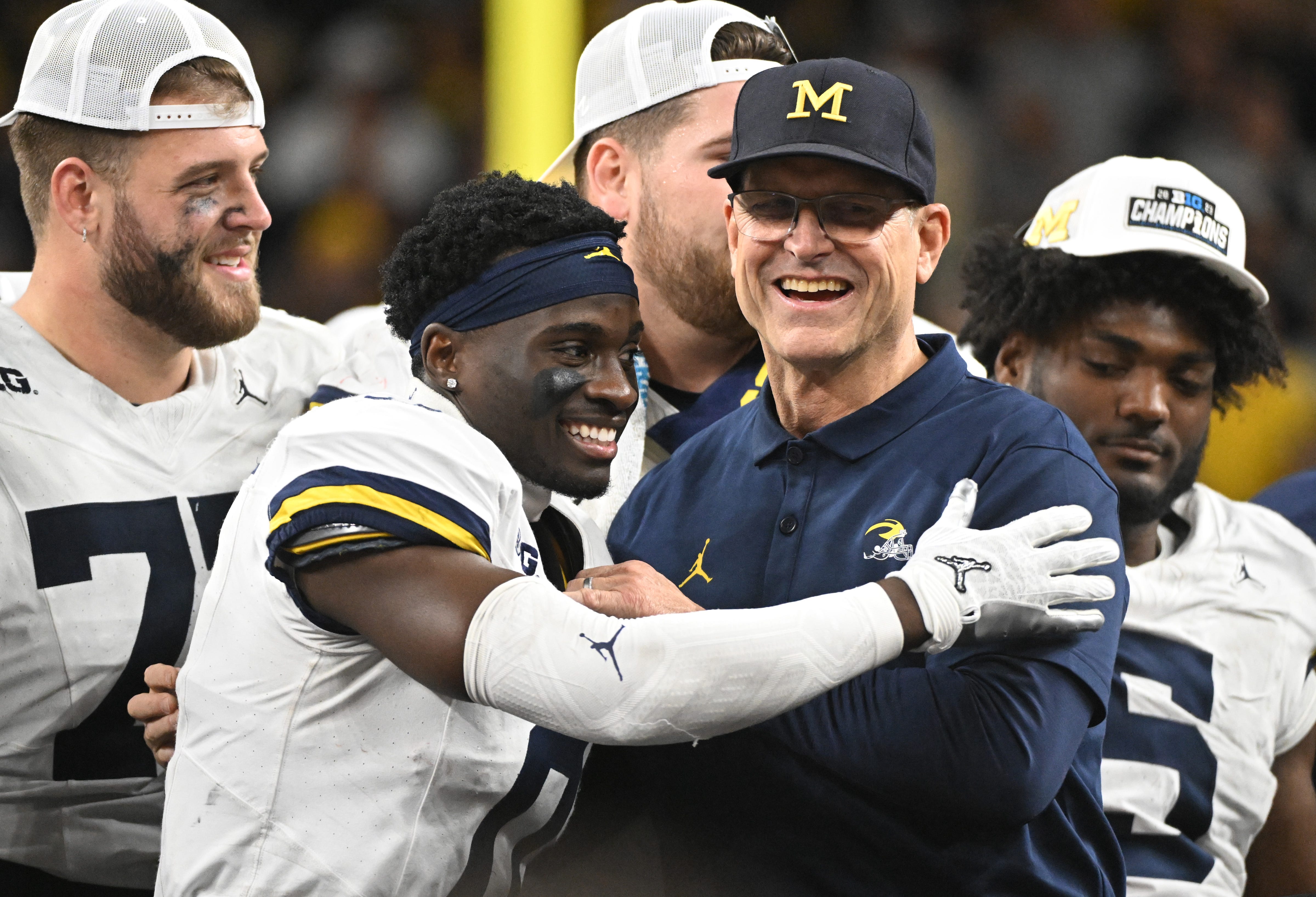 Michigan coach Jim Harbaugh celebrates with defensive back Mike Sainristil (0) after winning the Big Ten championship game against Iowa at Lucas Oil Stadium.