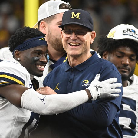 Michigan coach Jim Harbaugh celebrates with defensive back Mike Sainristil (0) after winning the Big Ten championship game against Iowa at Lucas Oil Stadium.
