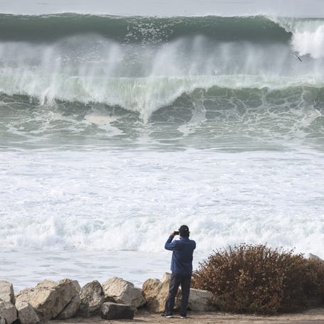 A person takes photos as large waves break near the beach on Friday, Dec. 29, 2023, in Manhattan Beach, California. Dangerous surf churned up by storms in the Pacific is impacting much of California's coastline with coastal flooding possible in some low-lying areas.