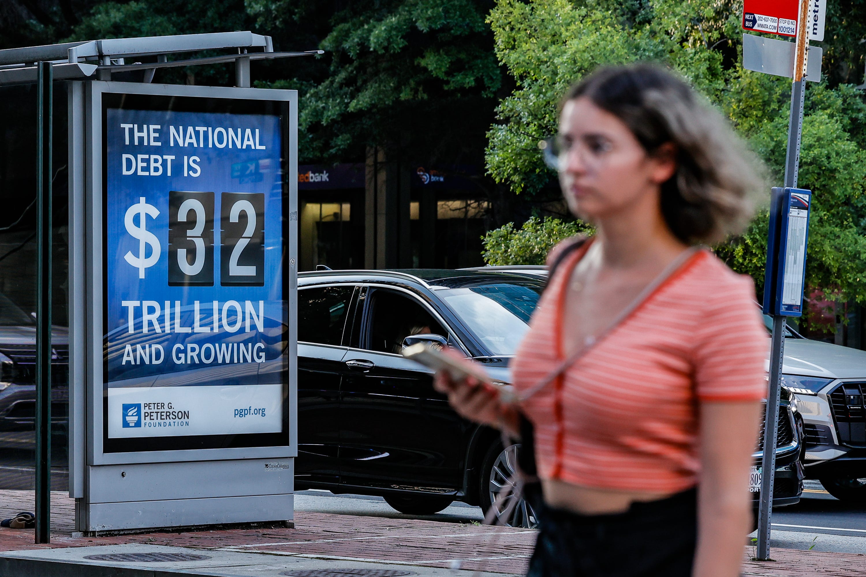 WASHINGTON, DC - JULY 06: Pedestrians walk past a poster and electronic billboard displayed at 18th and K St's NW that displays the current U.S. National debt per person and as a nation at 32 Trillion dollars on July 06, 2023 in Washington, DC.