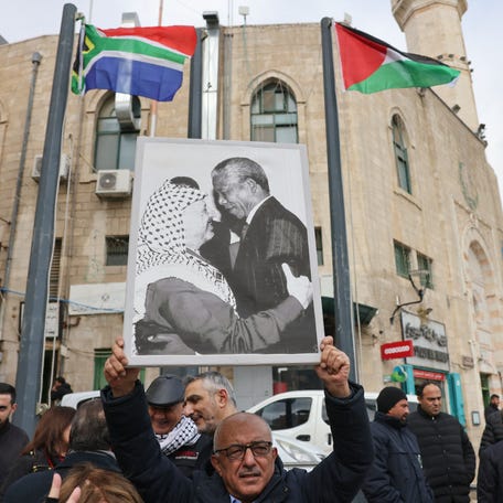 A Palestinian man holds a portrait of late Palestine Liberation Organisation leader Yasser Arafat and South Africa's anti-apartheid icon Nelson Mandela outside a municipality building in Bethlehem in the occupied West Bank, on Jan. 12, 2024.