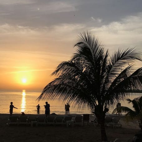 People are silhouetted on a beach at sunset in Negril, Jamacia on May 21, 2017.