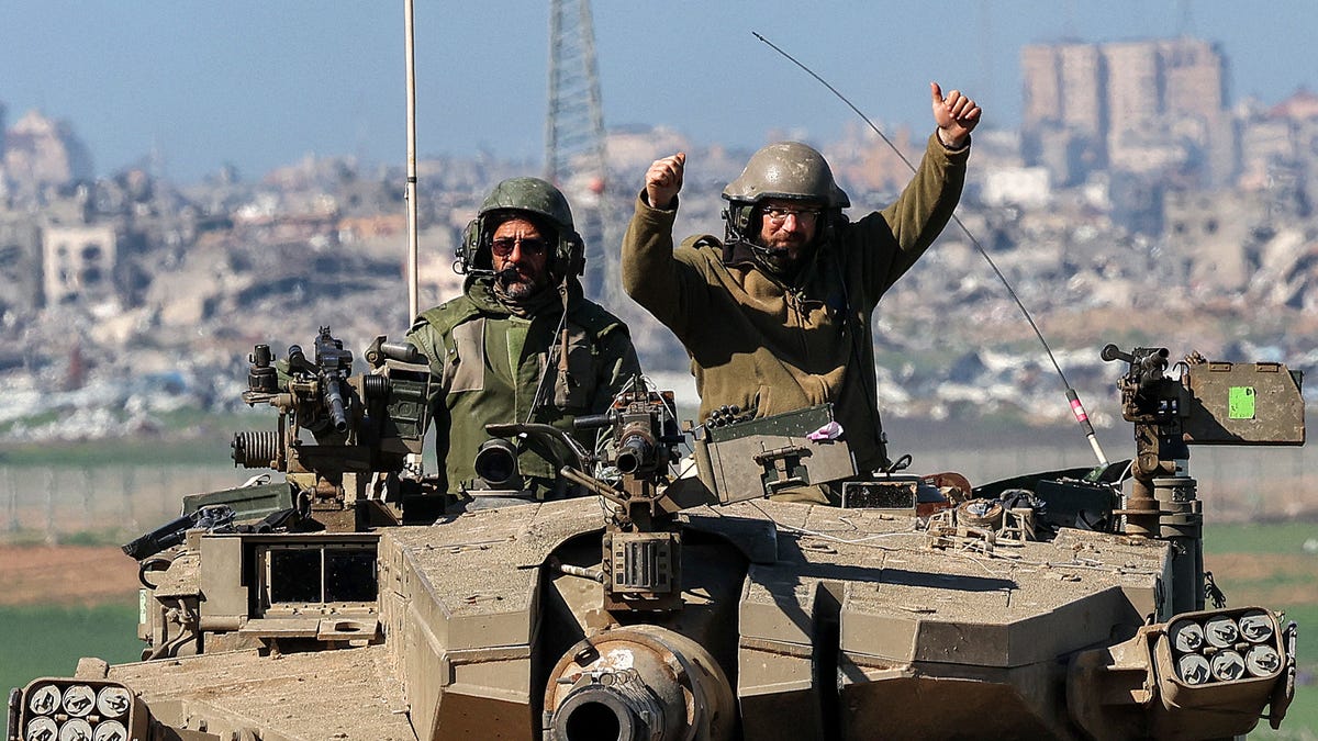 An Israeli army soldier gestures while seated in the turret of a battle tank moving at a position along the border between southern Israeli and the Gaza Strip on January 31, 2024.