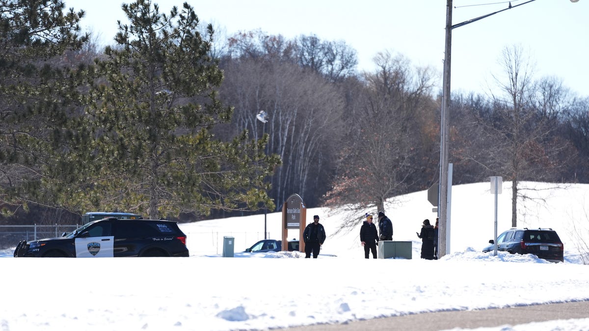 Law enforcement stand on a road after two police officers and a first responder were shot and killed Sunday, Feb. 18, 2024, in Burnsville, Minn.