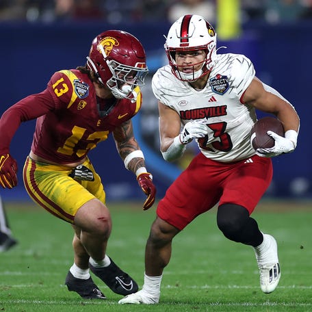 Isaac Guerendo #23 of the Louisville Cardinals rushes the ball past the defense of Mason Cobb #13 of the USC Trojans during the first half of the DIRECTV Holiday Bowl at Petco Park on December 27, 2023 in San Diego, California.