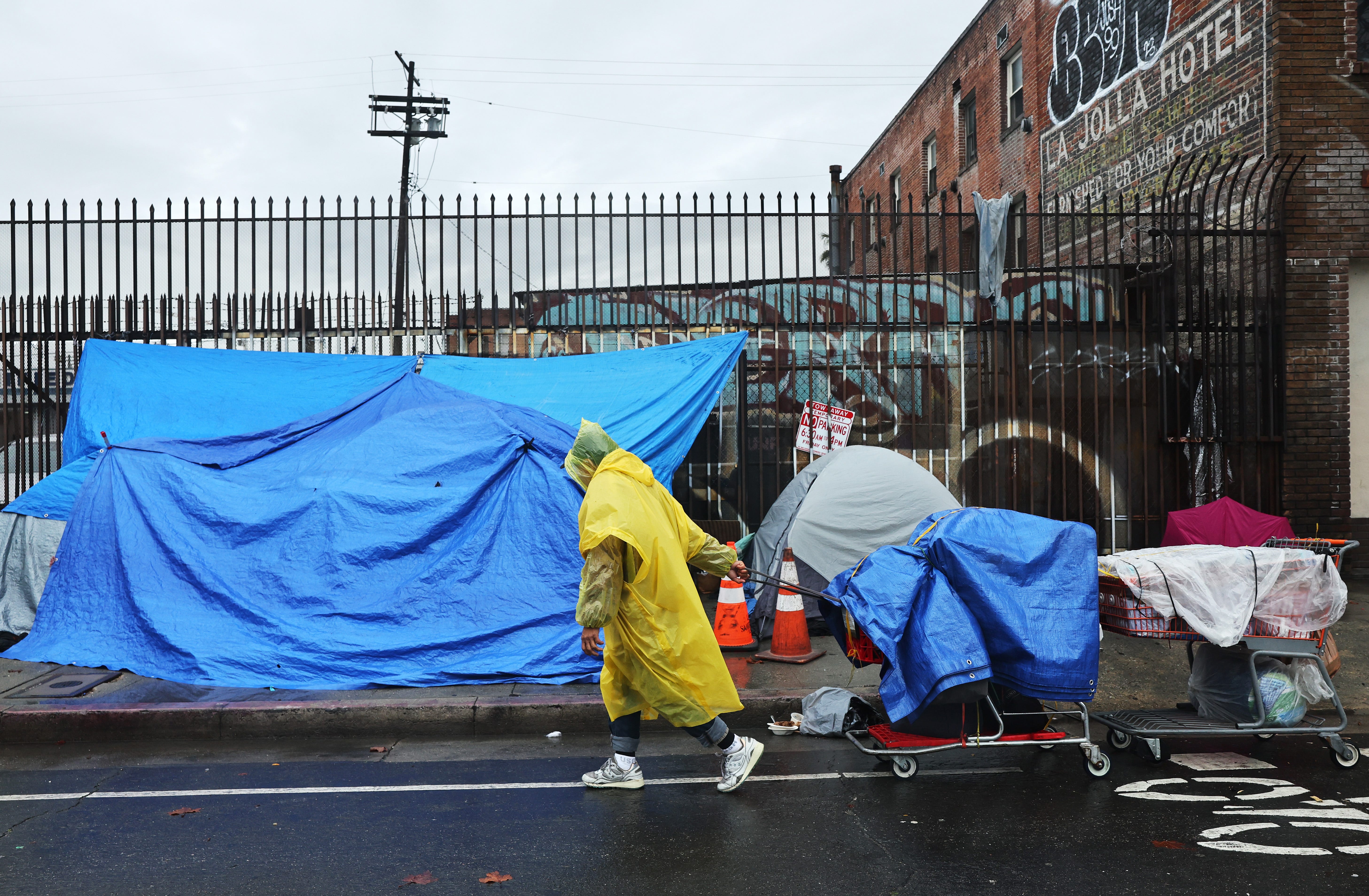 A person walks with carts in the rain near an encampment of unhoused people in Skid Row as a powerful long-duration atmospheric river storm, the second in less than a week, continues to impact Southern California on February 6, 2024 in Los Angeles, California. Over seven inches of rain have fallen in downtown Los Angeles during the storm, half the average yearly total. The storm delivered widespread flooding, landslides and power outages while dropping heavy rain and   snow across the region. Skid Row is home to thousands of people who are either experiencing homelessness on the streets or living in shelters.