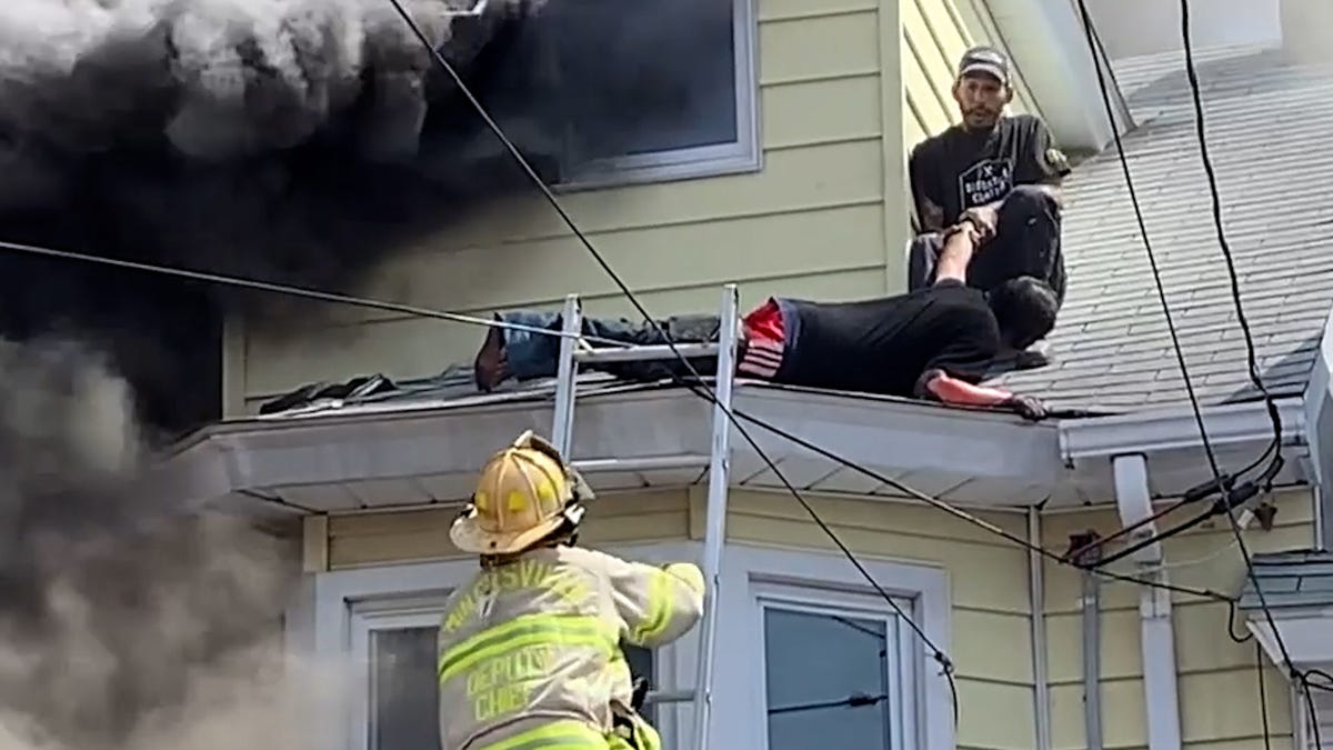 Oscar Rivera (right) is pictured after pulling the man (center) to safety from the house fire on April 14. A firefighter (left) is seen climbing up the ladder to get all three of the Minersville residents off the roof.