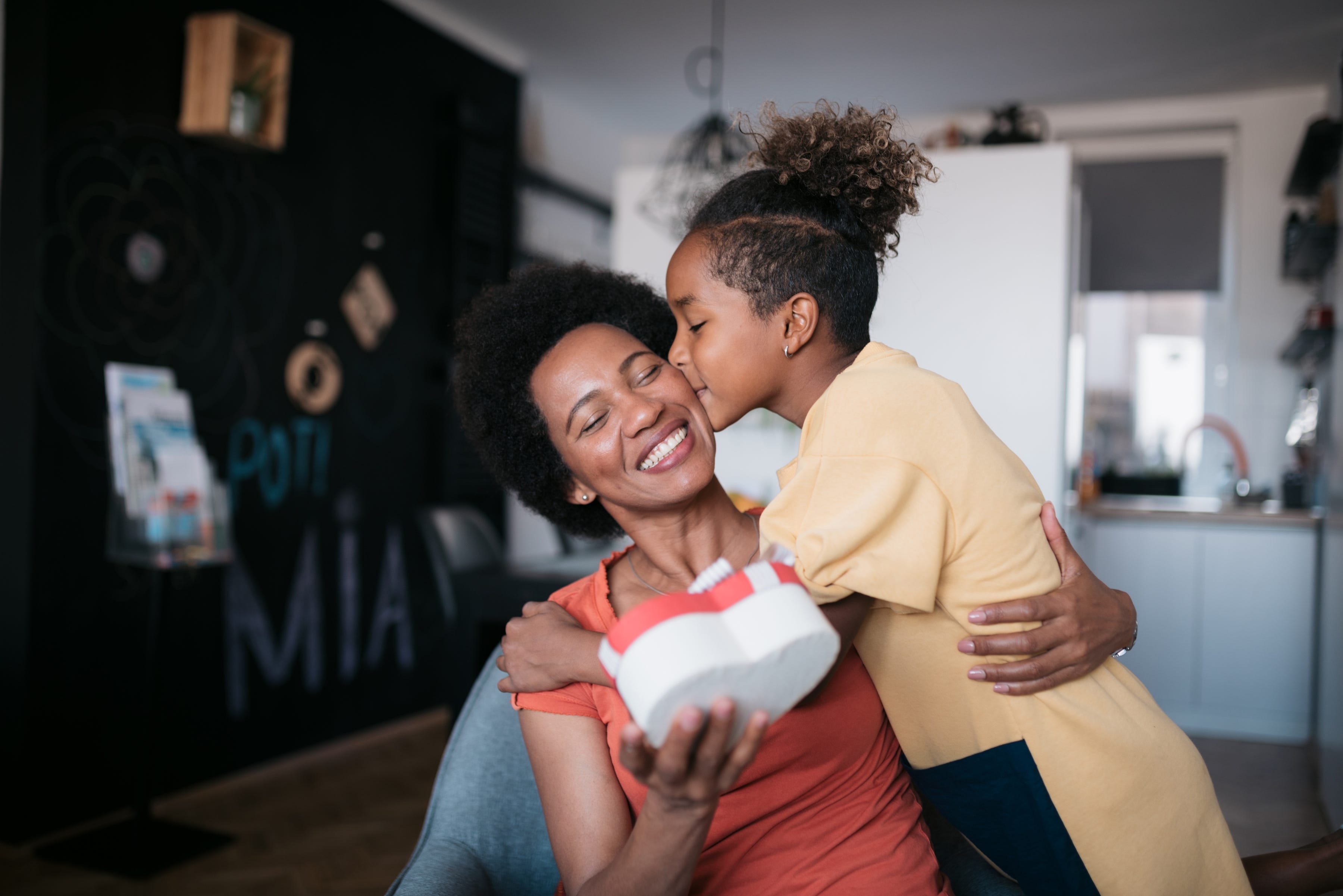 Young daughter surprising her mother at home with a nicely wrapped heart shaped giftbox on mother's day.