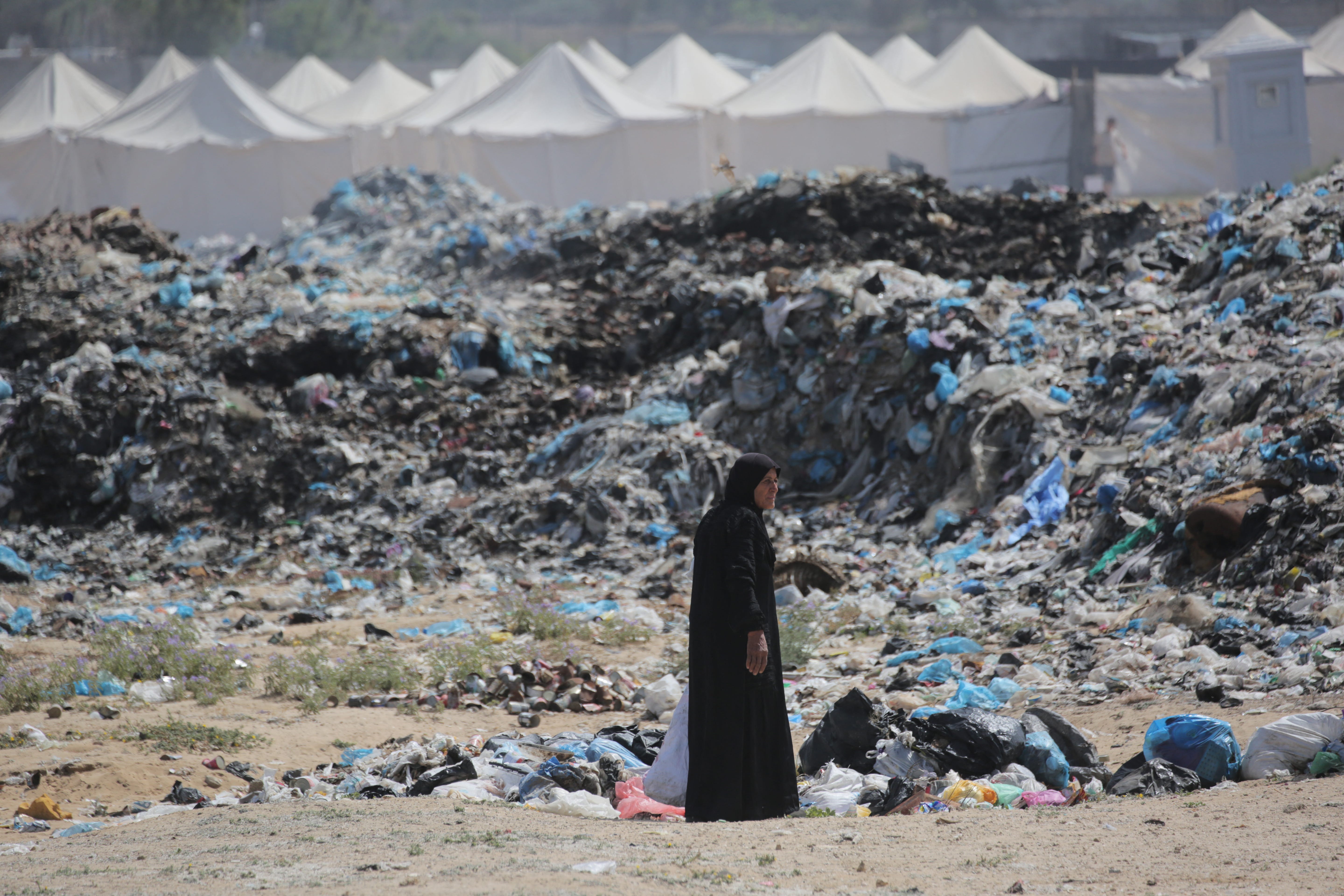 A woman salvages items from a waste dump expanding along a tent displacement camp west of Nuseirat in the Gaza Strip on May 21, 2024.