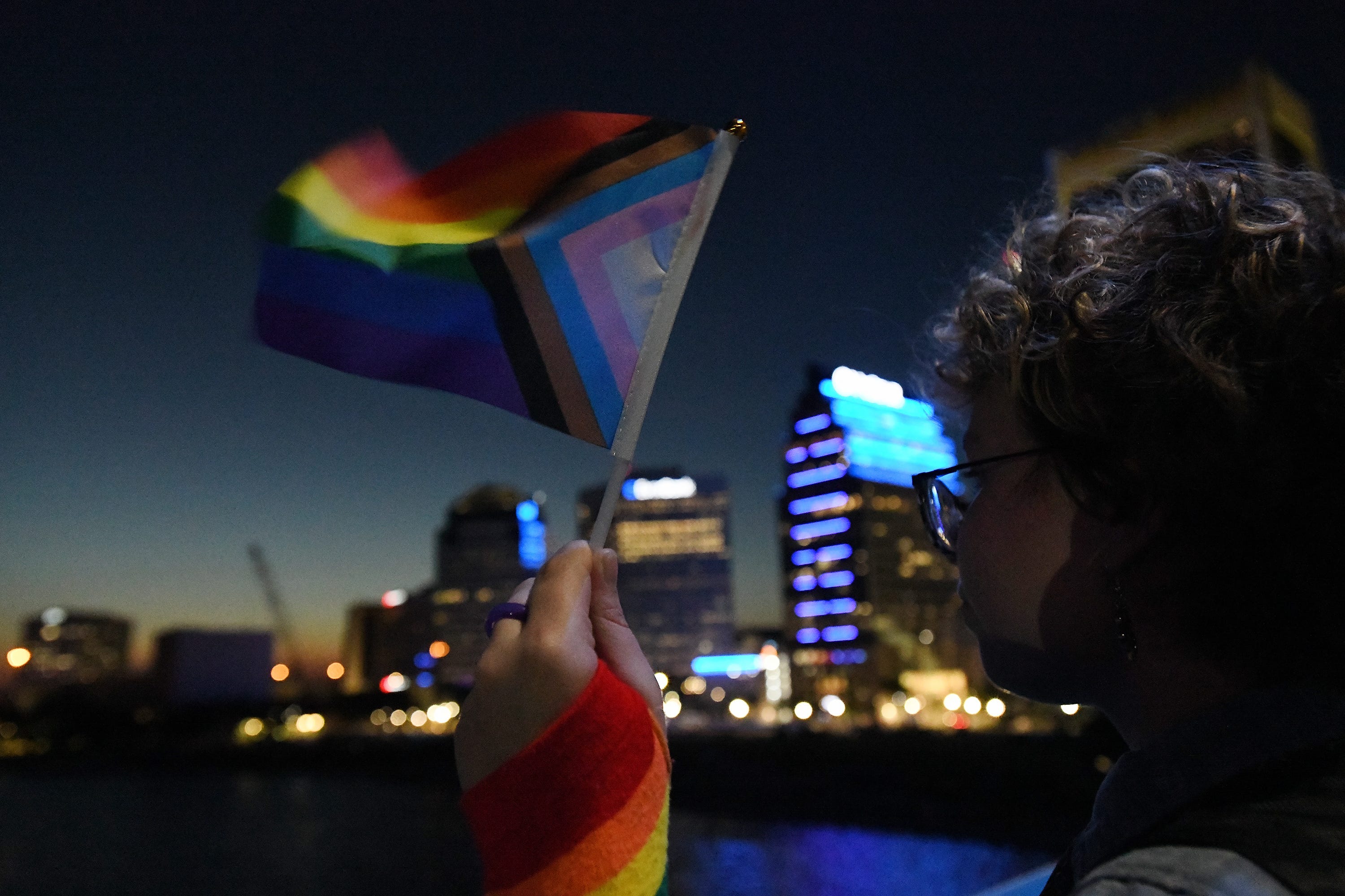 Clover Anglin holds a small LGBTQ Plus flag as he takes his position on the Main Street Bridge in preparation of lighting it in pride rainbow colors Friday night.
