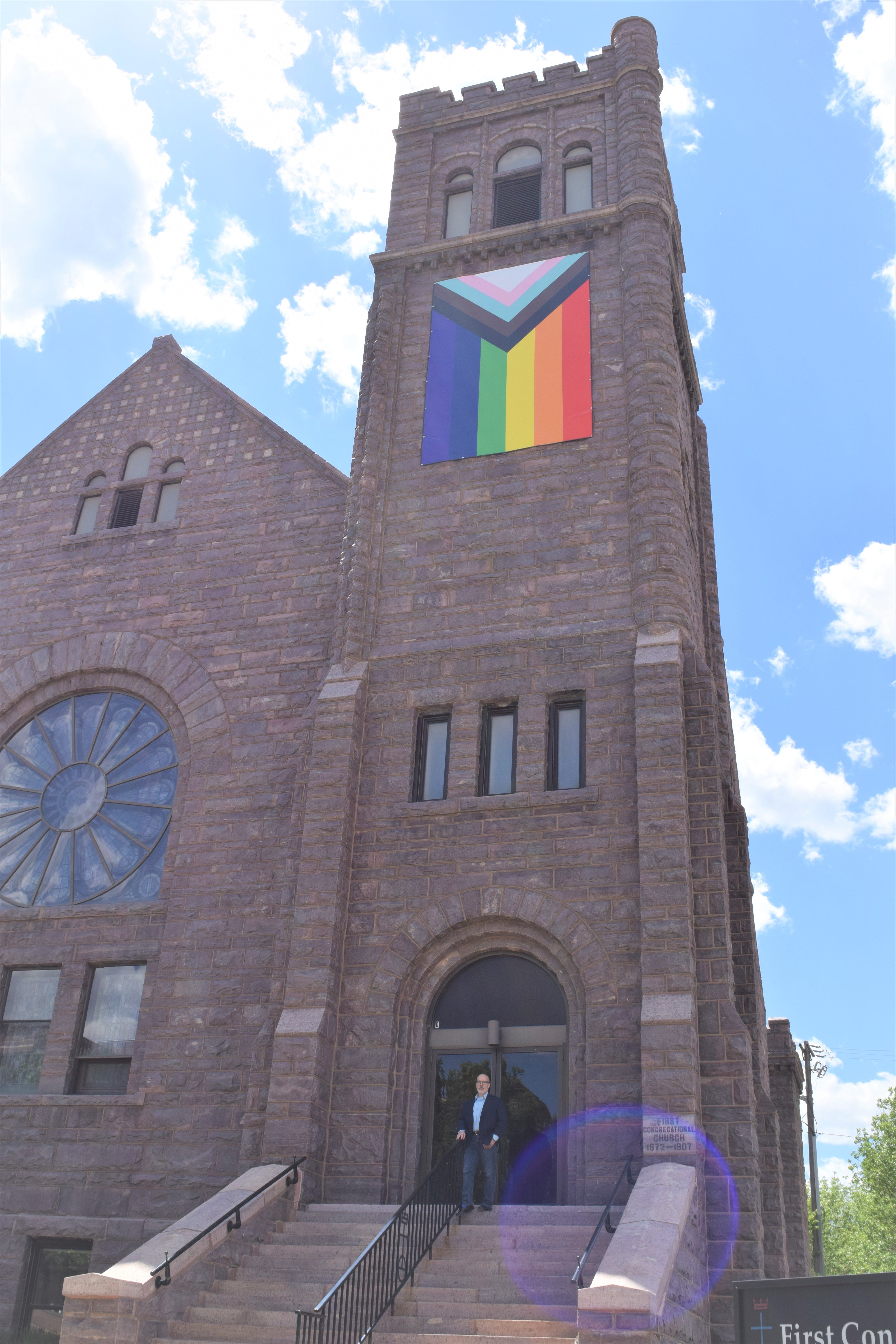Pastor Martell Spagnolo poses for a portrait outside First Congregational Church in downtown Sioux Falls on June 2, 2022. The church proudly displays a Progress pride flag, representing parts of the traditional gay rainbow flag, transgender pride flag in chevron and black and brown chevron stripes for people of color.