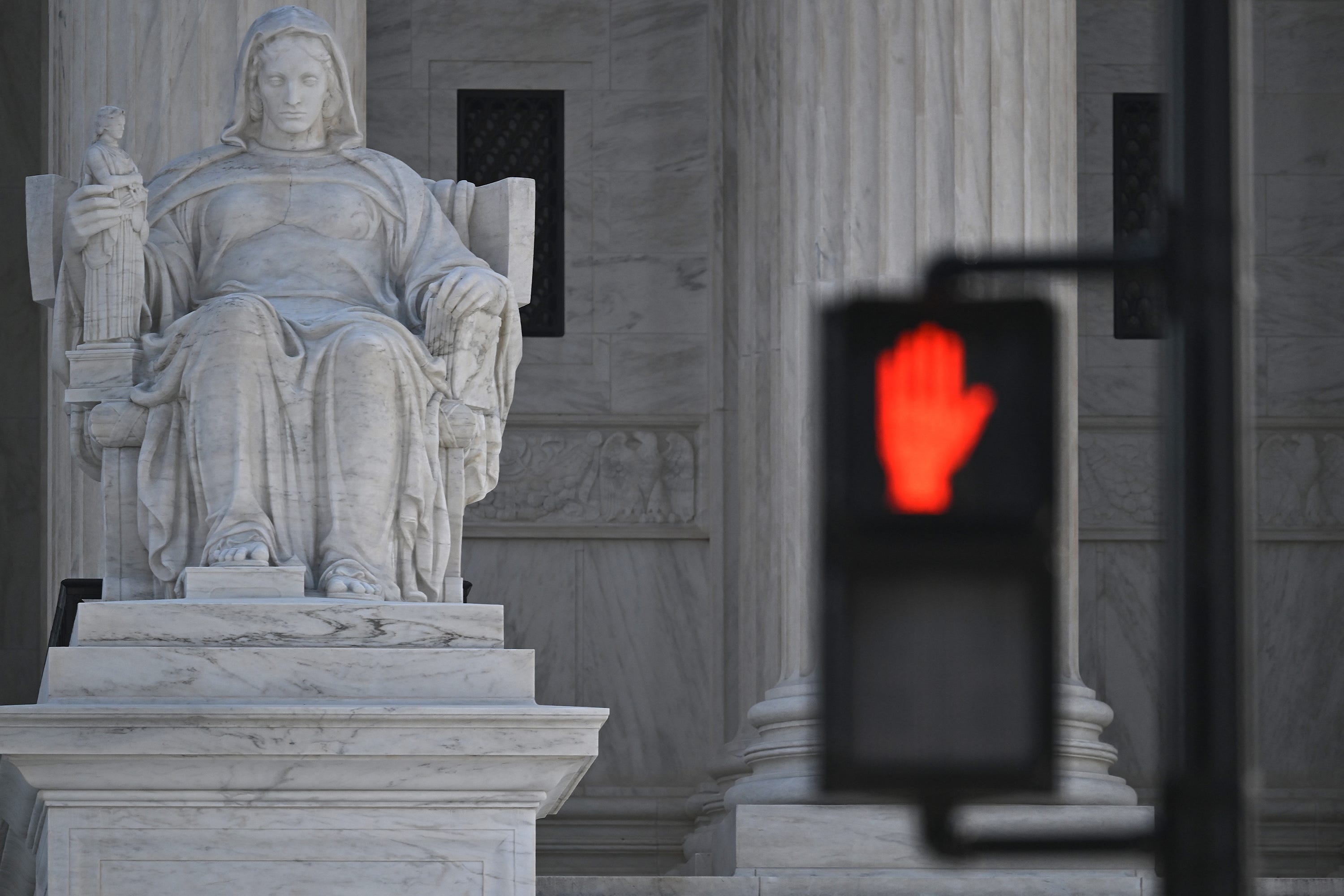 A stop sign as seen on traffic light near a statue at the Supreme Court in Washington, DC, February 26, 2024 as Justices are set to make a decision on landmark cases over social media content moderation. The Supreme Court on Monday will determine whether states can forbid social media companies from blocking or removing user content that goes against platform rules in the NetChoice v. Paxton and Moody v. NetChoice case. The state laws at issue also allow   individuals to sue tech companies for alleged violations.