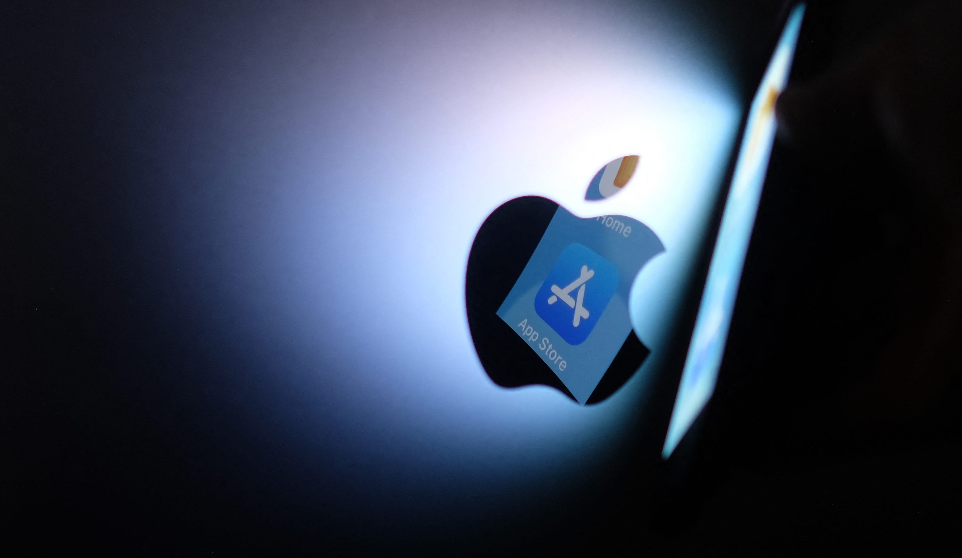 This illustration photo shows the Apple app store logo reflected from an iPhone onto the back of an iMac in Los Angeles, August 26, 2021. - Apple has agreed to loosen payment restrictions on its App Store, a major change announced in a settlement with small developers as the US technology giant faces growing scrutiny and legal challenges over its tightly controlled online marketplace. The change will allow small developers to inform their customers of   alternative payment options beyond the official App Store.