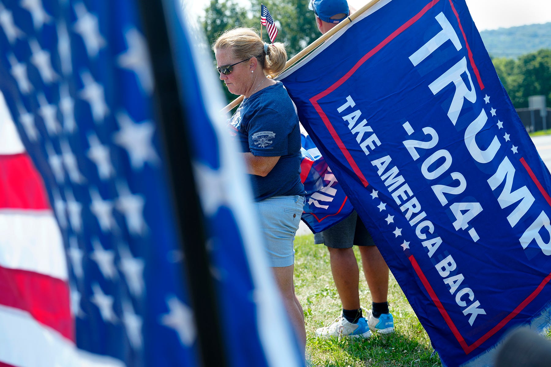 Lisa Burke, of New Vernon, holds a Trump flag near the intersection of Route 206 and Lamington Road, Sunday, July 14, 2024, in Bedminster.