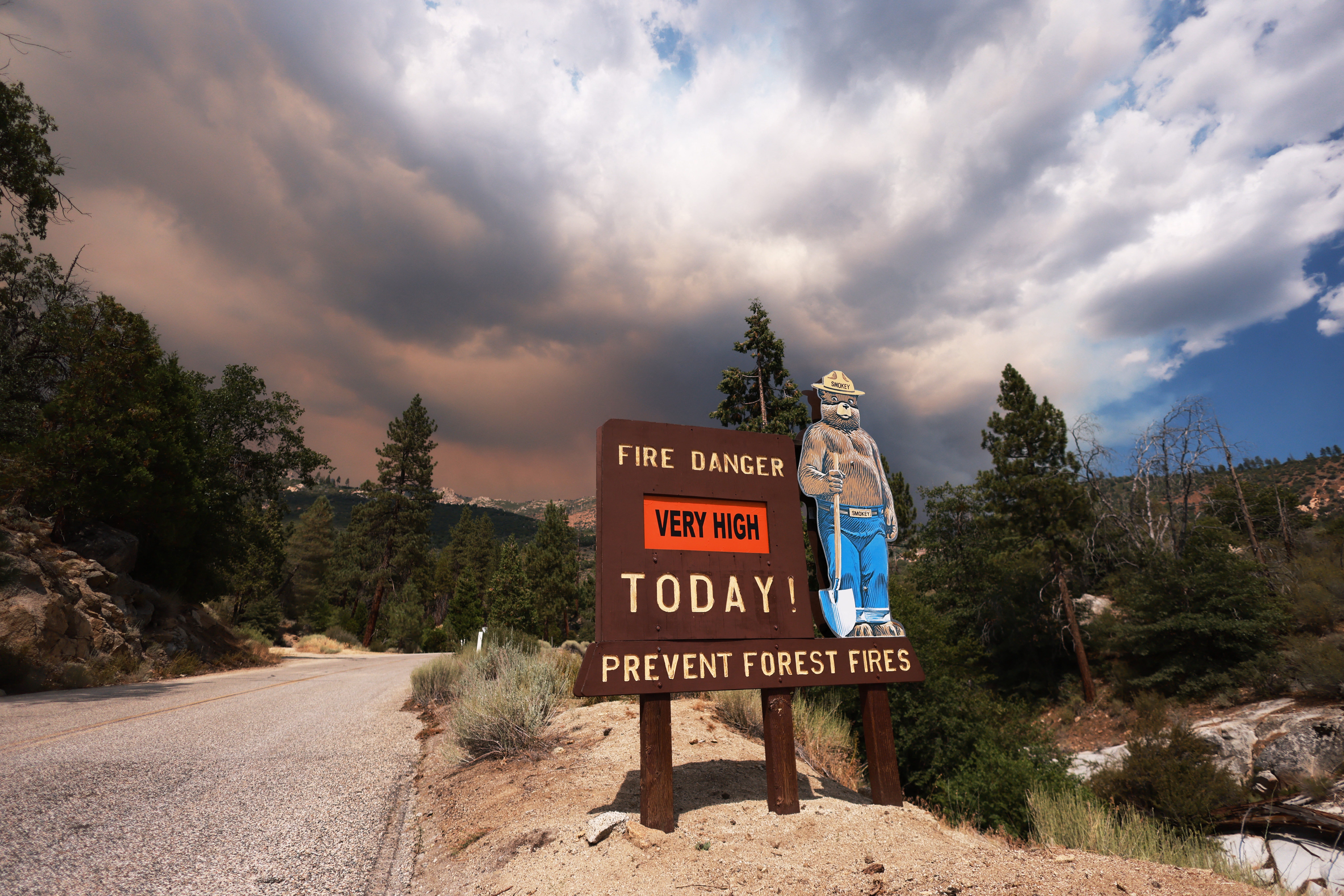 A sign with Smokey the Bear warns of a very high fire danger for the day as smoke rises from the Trout Fire burning in the Domeland Wilderness of Sequoia National Forest, near Inyokern, California, July 19, 2024. The fire has burned approximately 6,000 acres and is at 0% containment, according to Cal Fire.