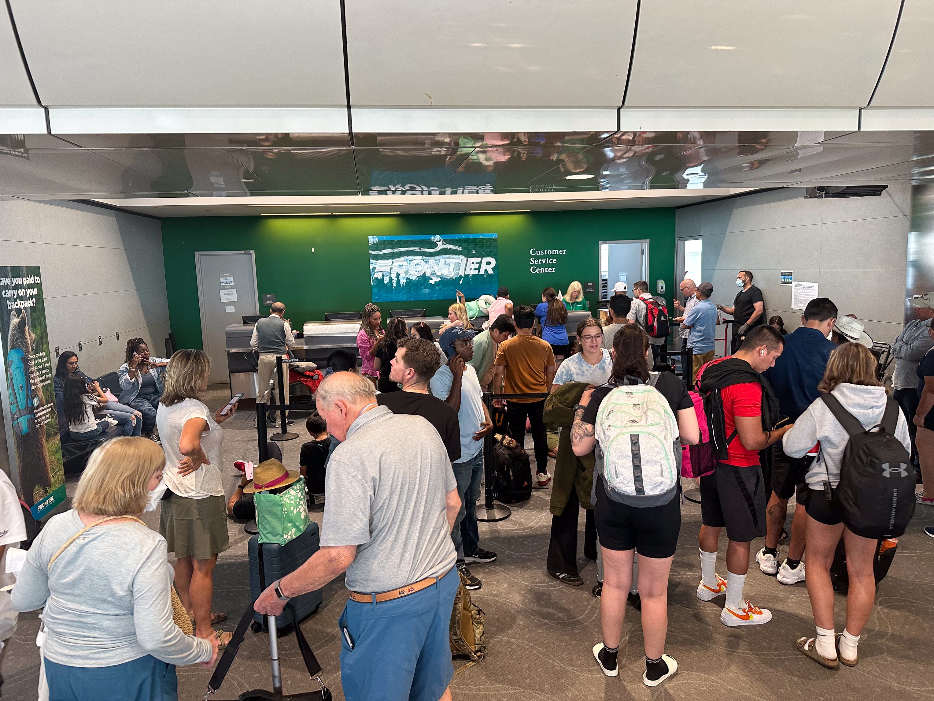 Frontier passengers cluster around customer service desk during the summer travel season at Denver International Airport.