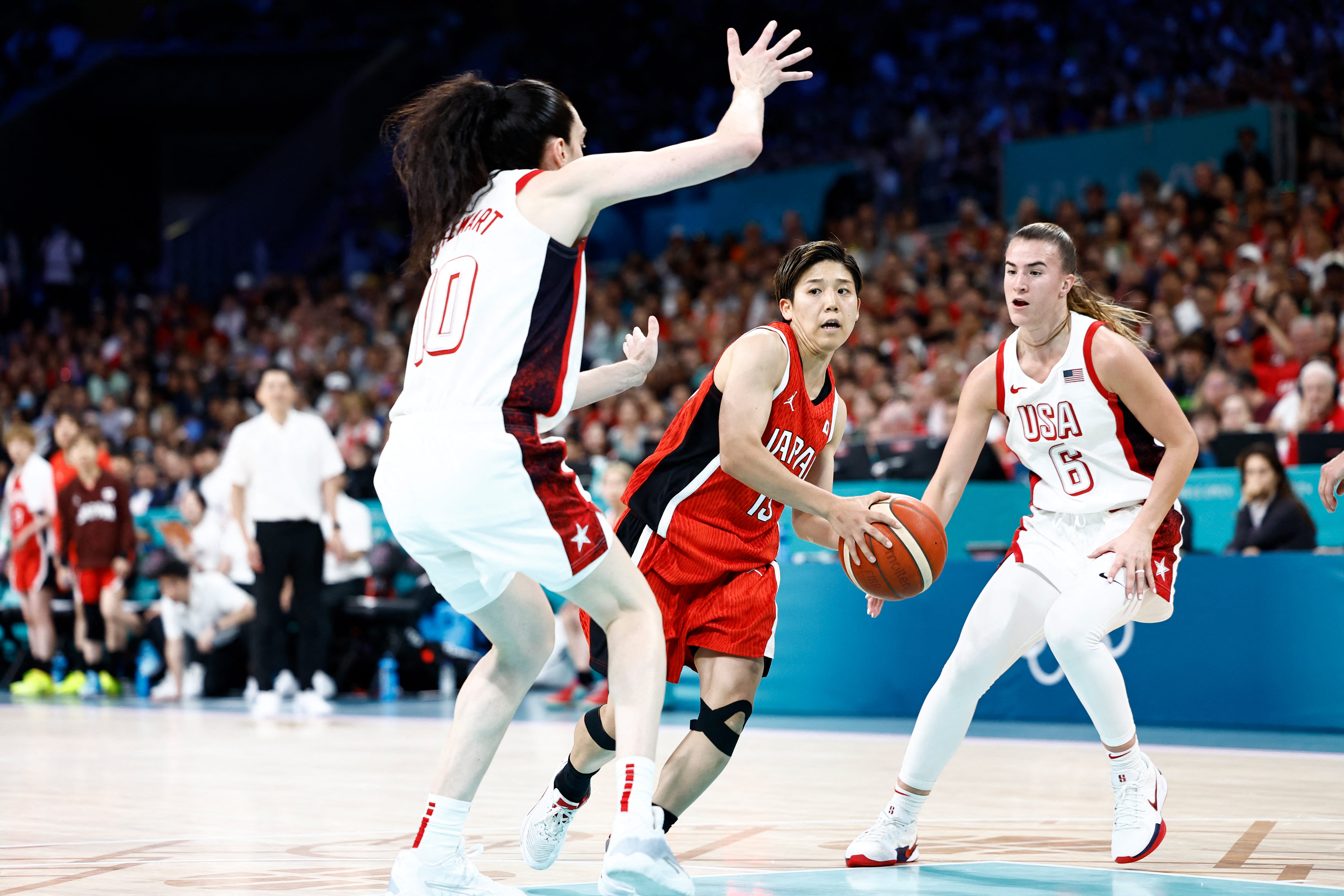 Japan's Rui Machida drives against Team USA's Breanna Stewart, left, and Sabrina Ionescu during the women's preliminary round at the Paris Olympics at the Pierre-Mauroy Stadium in Villeneuve-d'Ascq, France on July 29, 2024.