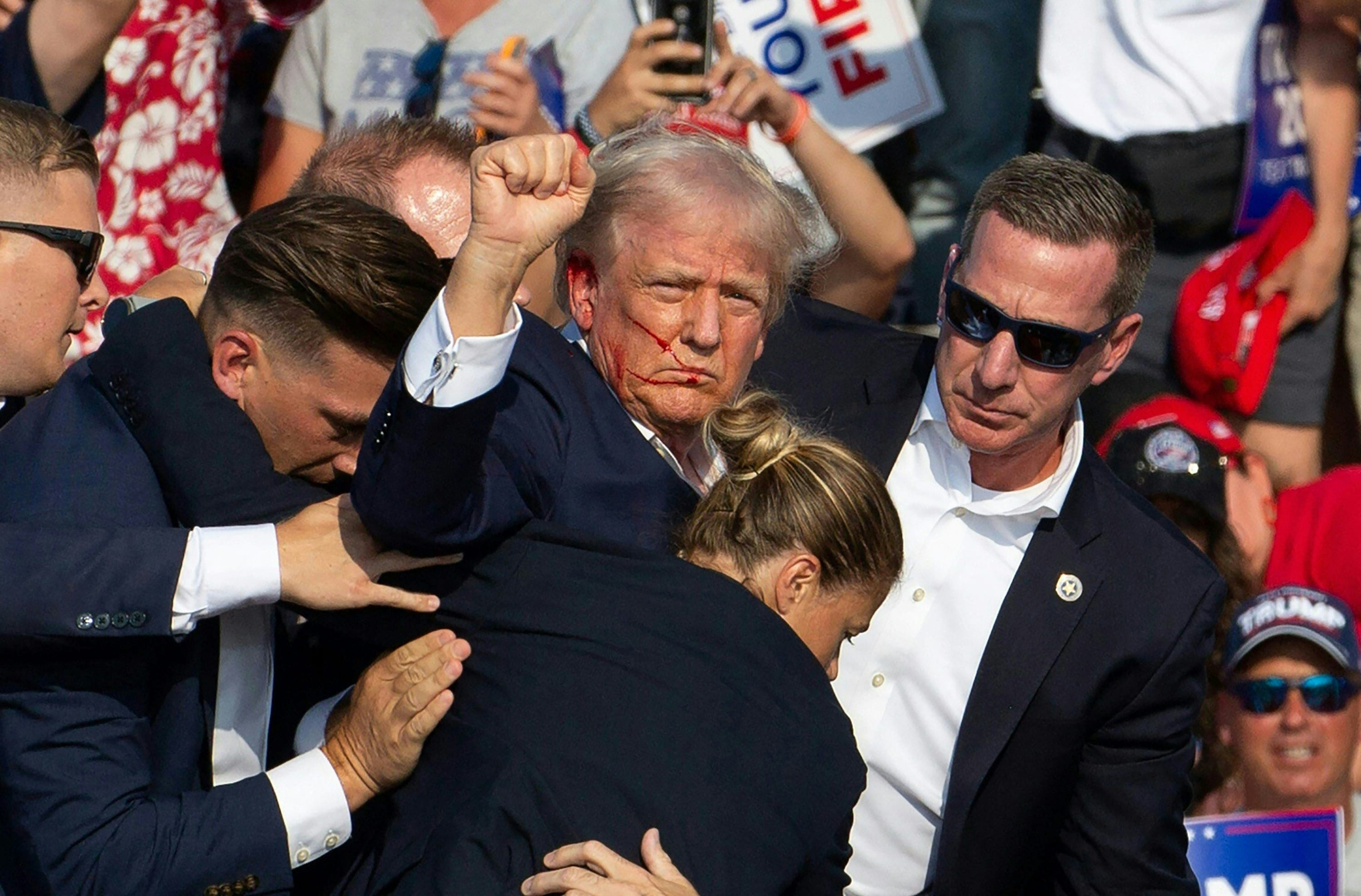 TOPSHOT - Republican candidate Donald Trump is seen with blood on his face surrounded by secret service agents as he is taken off the stage at a campaign event at Butler Farm Show Inc. in Butler, Pennsylvania, July 13, 2024. Donald Trump was hit in the ear in an apparent assassination attempt by a gunman at a campaign rally on Saturday, in a chaotic and shocking incident that will fuel fears of instability ahead of the 2024 US presidential election.  The 78-year-old former president was rushed off stage with blood smeared across his face after the shooting in Butler, Pennsylvania, while the gunman and a bystander were killed and two spectators critically injured. (Photo by Rebecca DROKE / AFP) (Photo by REBECCA DROKE/AFP via Getty Images)