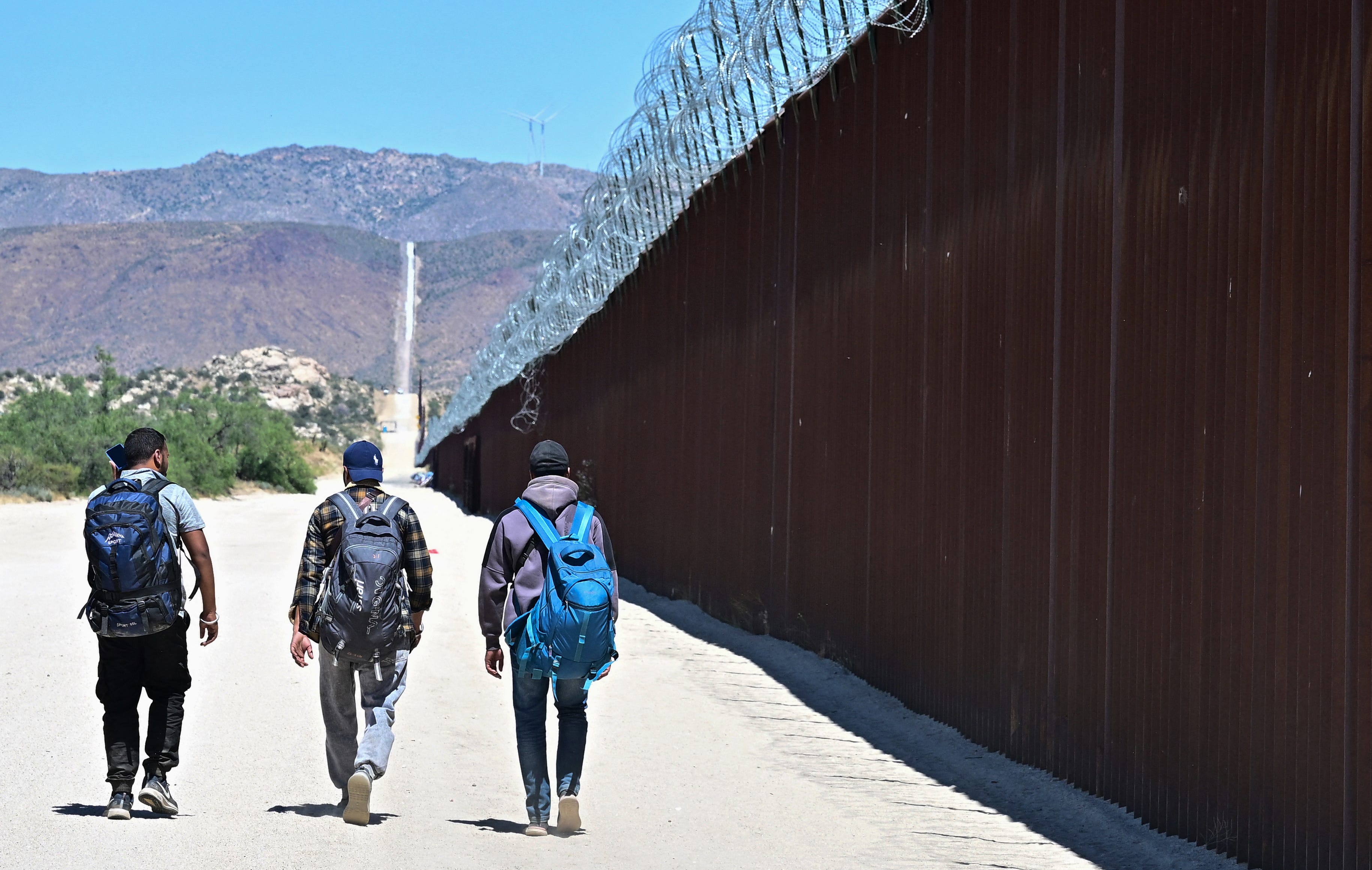 Migrants walk on the US side of the border wall in Jacumba Hot Springs, California on June 5, 2024, after walking crossing from Mexico. Migrants from countries such as Turkey, Jordan, Guatemala, Nicaragua, China and India made their way on foot into the United States today before being met with by Customs and Border Patrol agents for processing. The United States will temporarily close its Mexico border to asylum seekers starting today, June 5, as President Joe Biden as   tries to neutralize his political weakness on migration ahead of November's election battle with Donald Trump.  The 81-year-old Democrat signed a long-awaited executive order taking effect at midnight to "gain control" of the southern frontier with Mexico, after record numbers of illegal border crossings sparked concerns among voters. (Photo by Frederic J. BROWN / AFP) (Photo by FREDERIC J. BROWN/AFP via Getty Images)