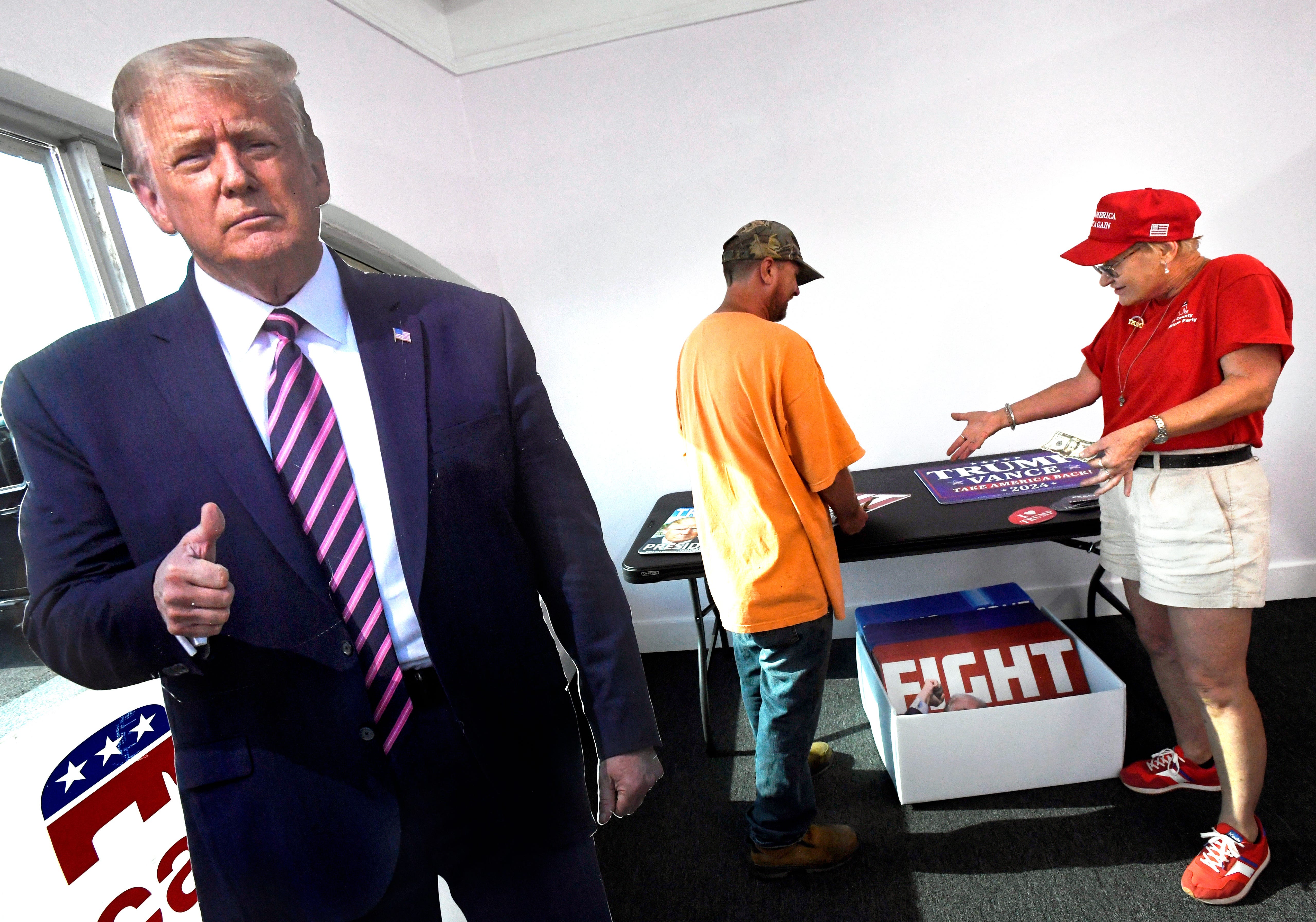 Darla Avery, a precinct chair and the Action Committee chair for the Taylor County Republican Party, offers a supporter the selections for purchasing a Donald Trump election yard sign at the partyâ€™s headquarters Saturday Aug. 24, 2024. Standard signs go for $5. The one featuring a bloodied Trump beneath the word "Fight" sells for $10. The office has several live-sized cutouts of the former president available for selfie photos.