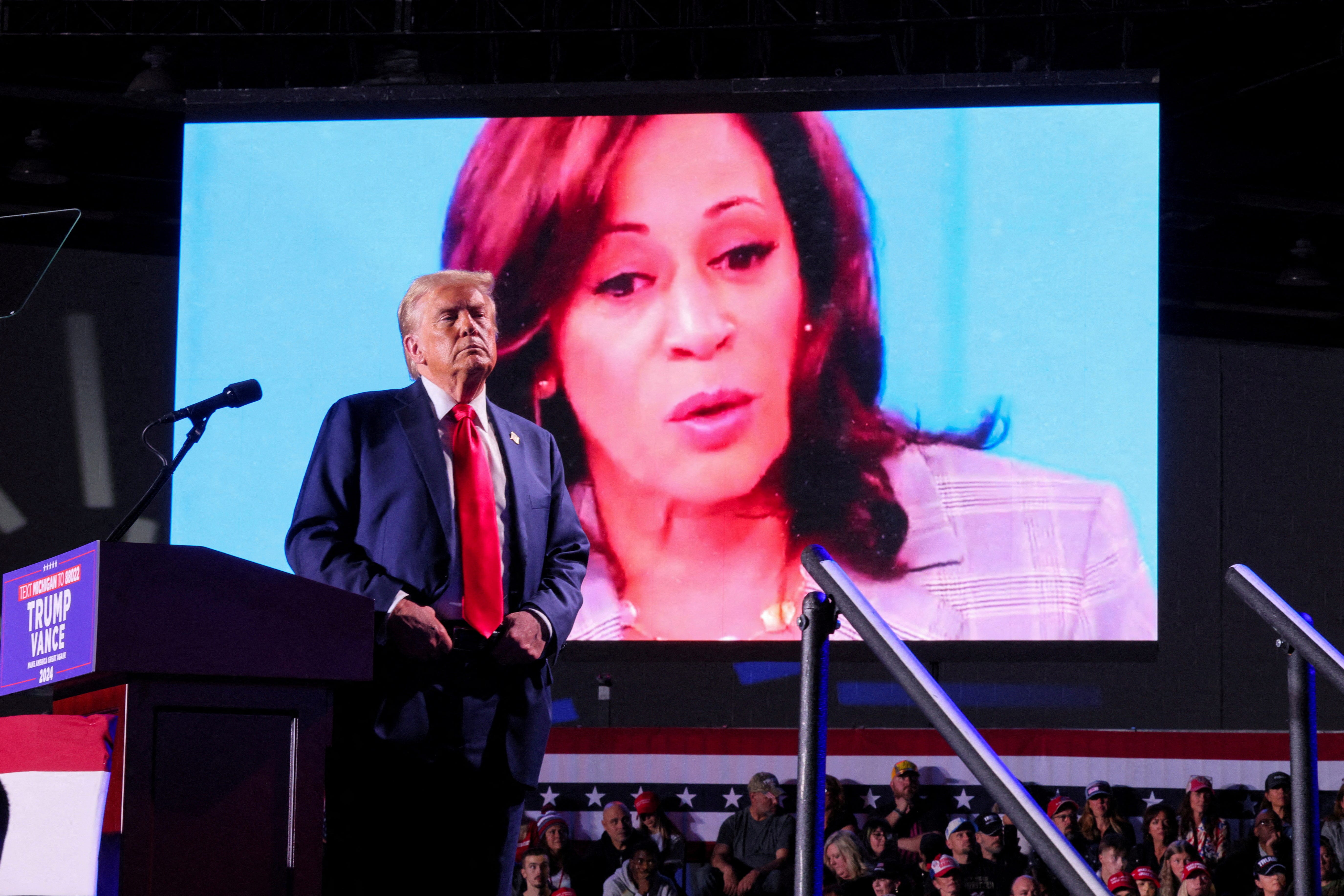 FILE PHOTO: Republican presidential nominee and former U.S. President Donald Trump looks on as Democratic presidential nominee and U.S. Vice President Kamala Harris' face appears as a video plays on a screen, during a rally at Huntington Place in Detroit, Michigan, U.S. October 18, 2024. REUTERS/Brian Snyder/File Photo