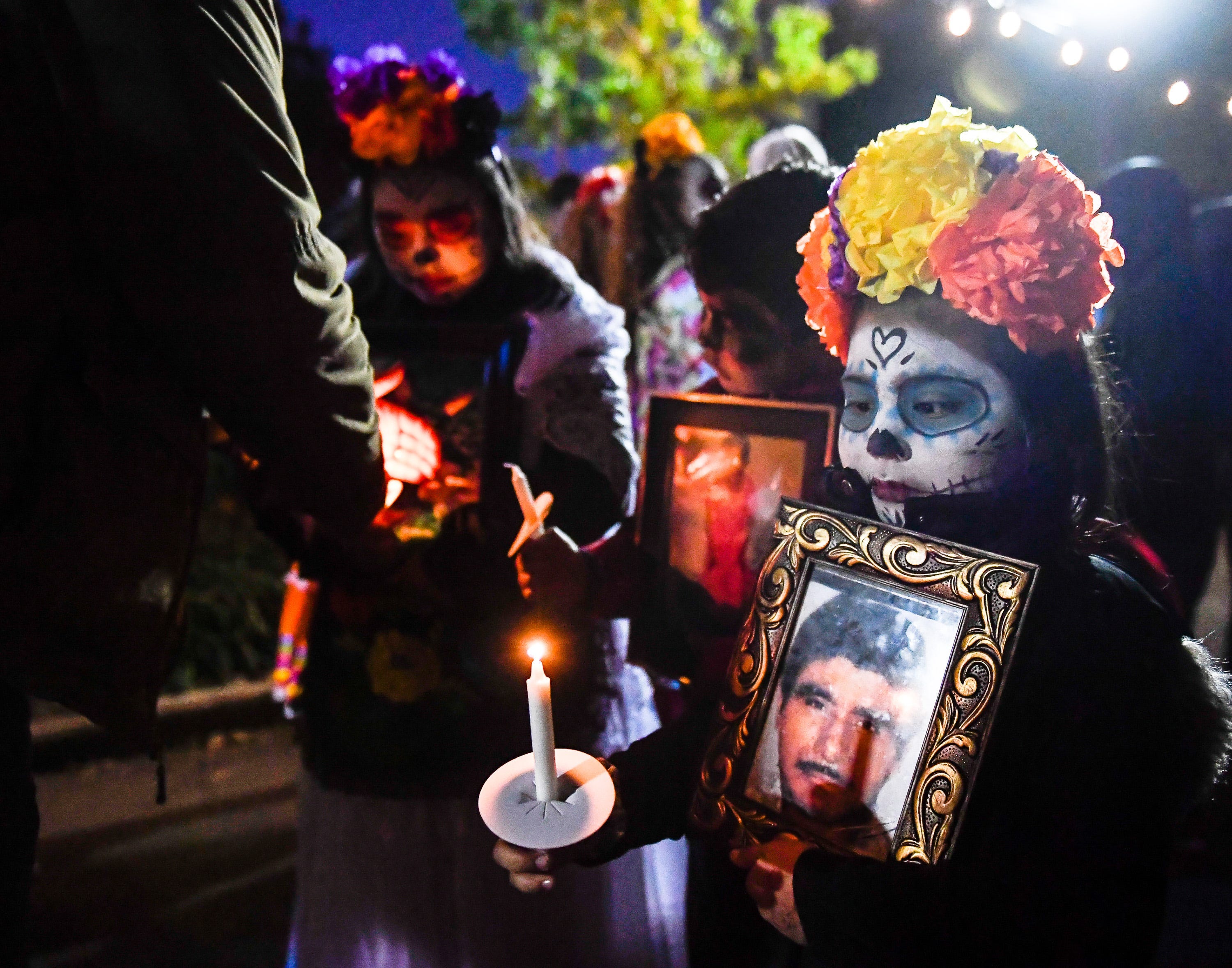 Lizbeth Arroyo holds a portrait of her grandfather as she prepares for a Dia de Los Muertos candlelight procession at Central Park in Henderson, Ky., in November 2019. The vibrant Mexican tradition celebrates the lives of lost loved ones with food, drink and celebration.