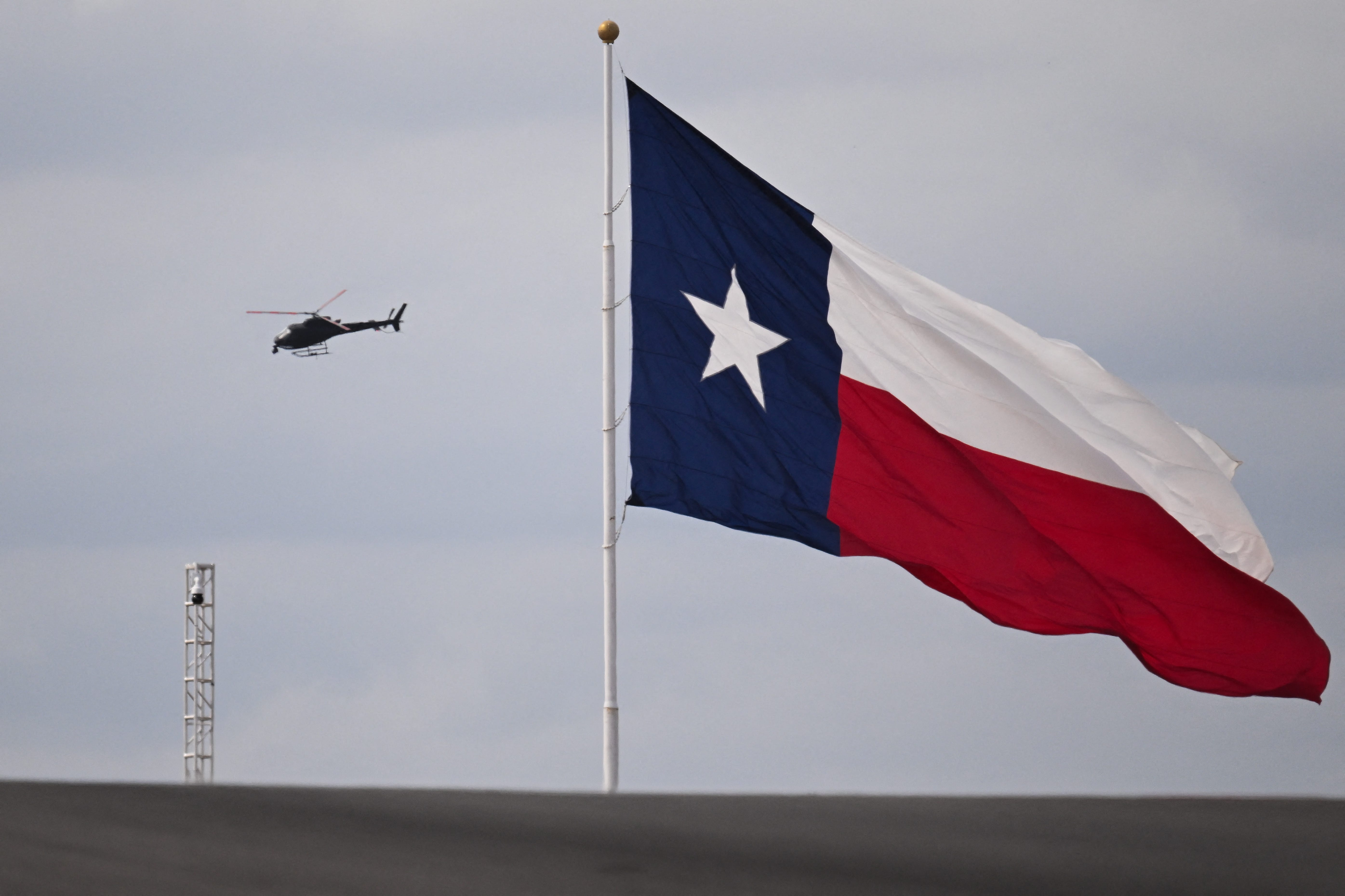 Red Bull pilot Aaron Fitzgerald flies the an AStar AS350 helicopter past the Texas state flag while filming a practice session for the United States Formula One Grand Prix at the Circuit of the Americas in October 18, 2024 in Austin, Texas. (Photo by Patrick T. Fallon / POOL / AFP) (Photo by PATRICK T. FALLON/POOL/AFP via Getty Images) ORG XMIT: 776090953 ORIG FILE ID: 2179117763
