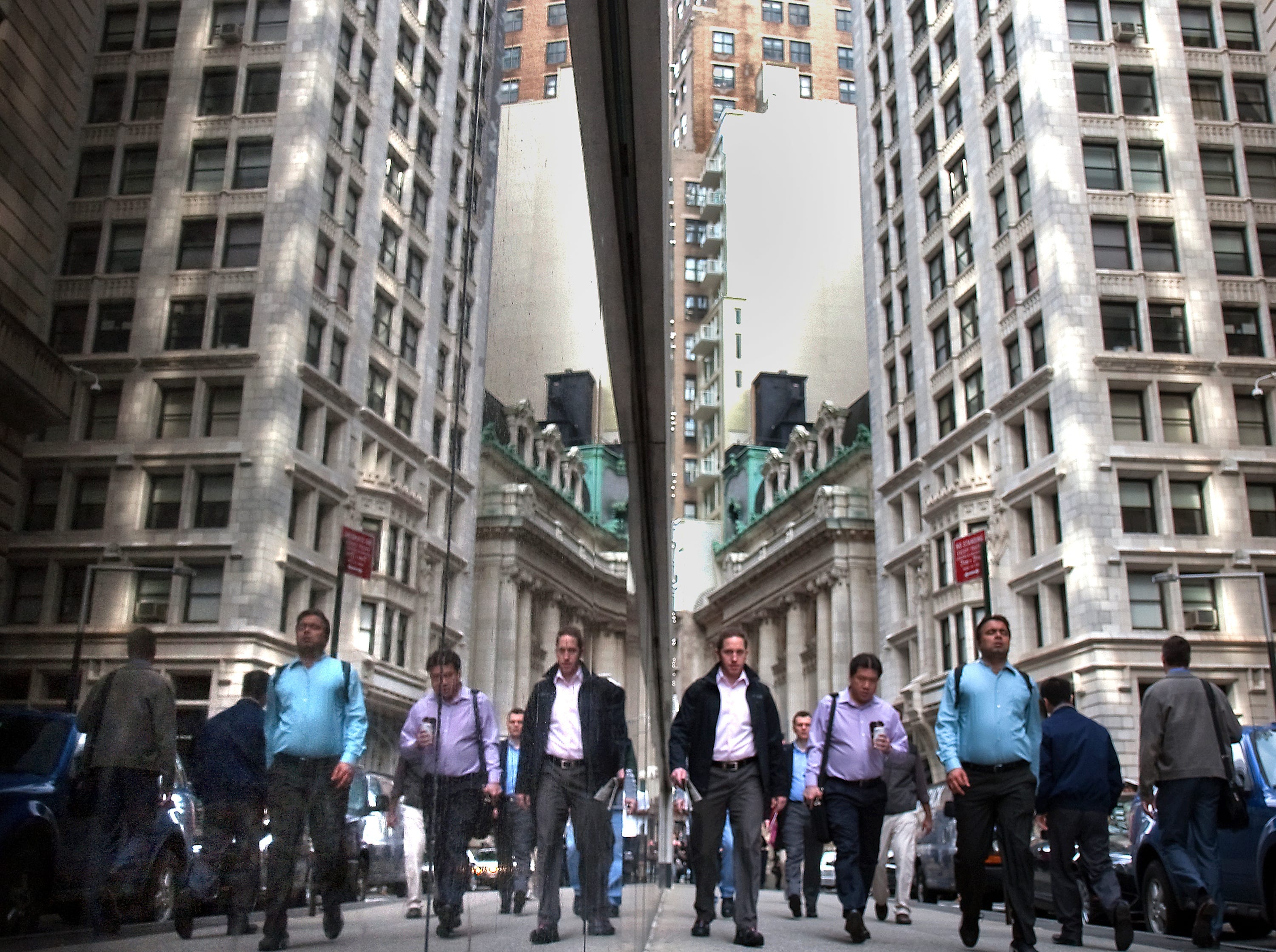 People are reflected in the polished black marble walls of a building, left, as they walk to work on Liberty Street in the financial district of Manhattan, New York on Jun. 21, 2013.