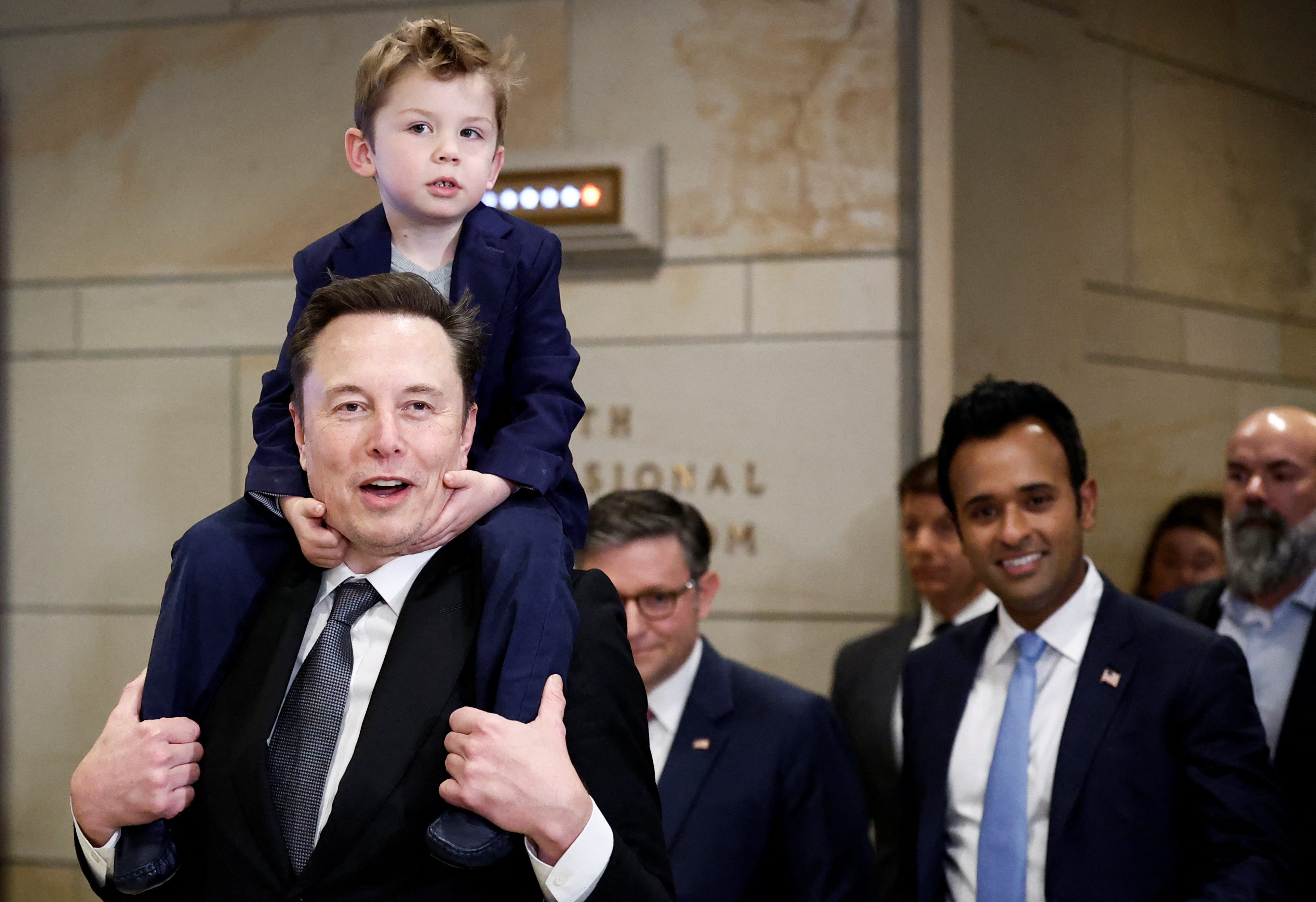 Elon Musk and Vivek Ramaswamy, who are leading President-elect Donald Trump's proposed new Department of Government Efficiency, walk on Capitol Hill on the day of a meeting with members of Congress, as Musk holds his son on his shoulders, on Dec. 5, 2024.