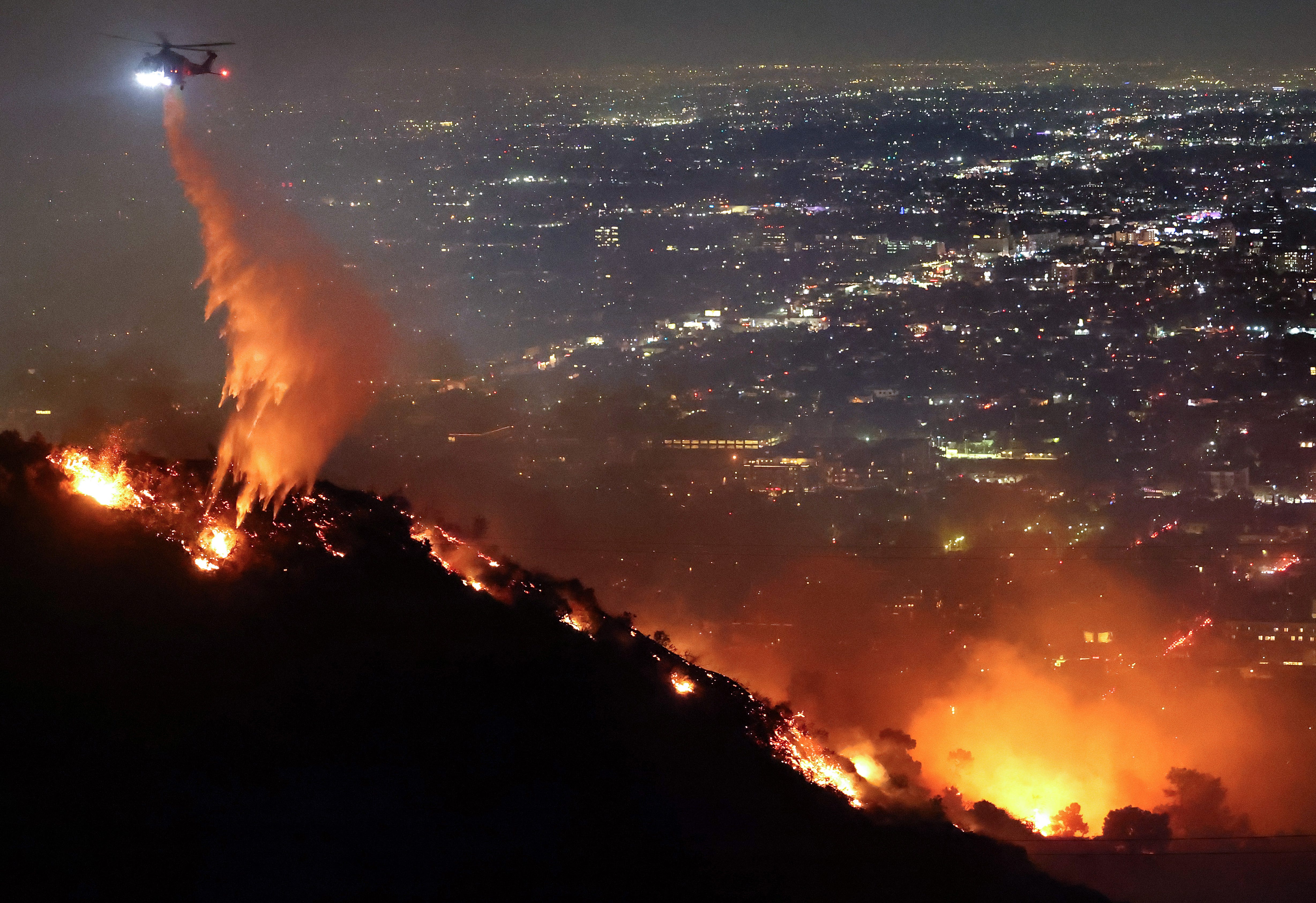 A firefighting helicopter drops water as the Sunset Fire burns in the Hollywood Hills with evacuations ordered on January 8, 2025 in Los Angeles, California. Over 1,000 structures have burned in multiple fires, with at least five people dead, in wildfires fueled by intense Santa Ana Winds across L.A. County.