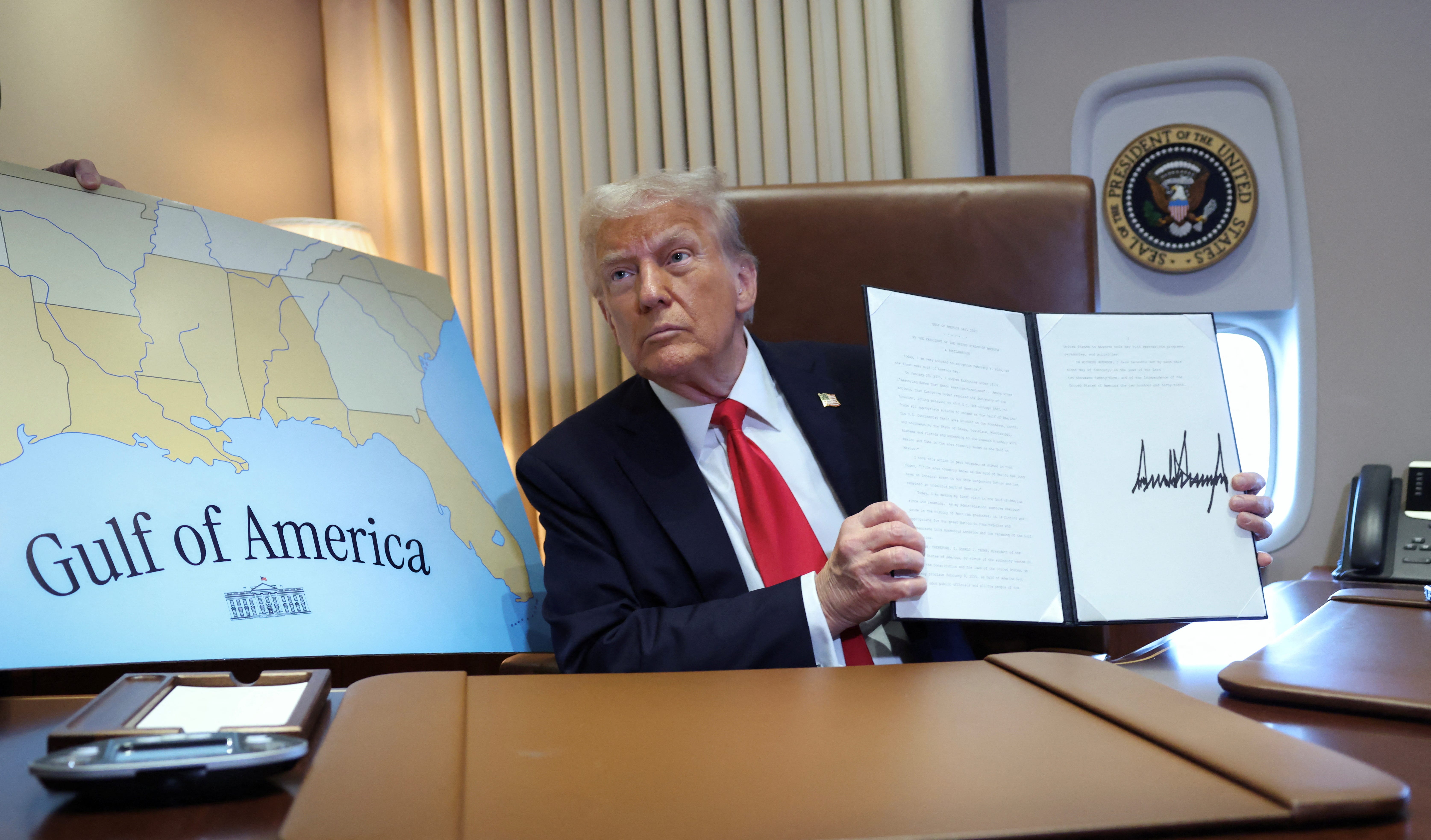 U.S. President Donald Trump holds up a proclamation renaming the Gulf of Mexico to the Gulf of America, while flying over the gulf aboard Air Force One en route to New Orleans to attend the Super Bowl, February 9, 2025.