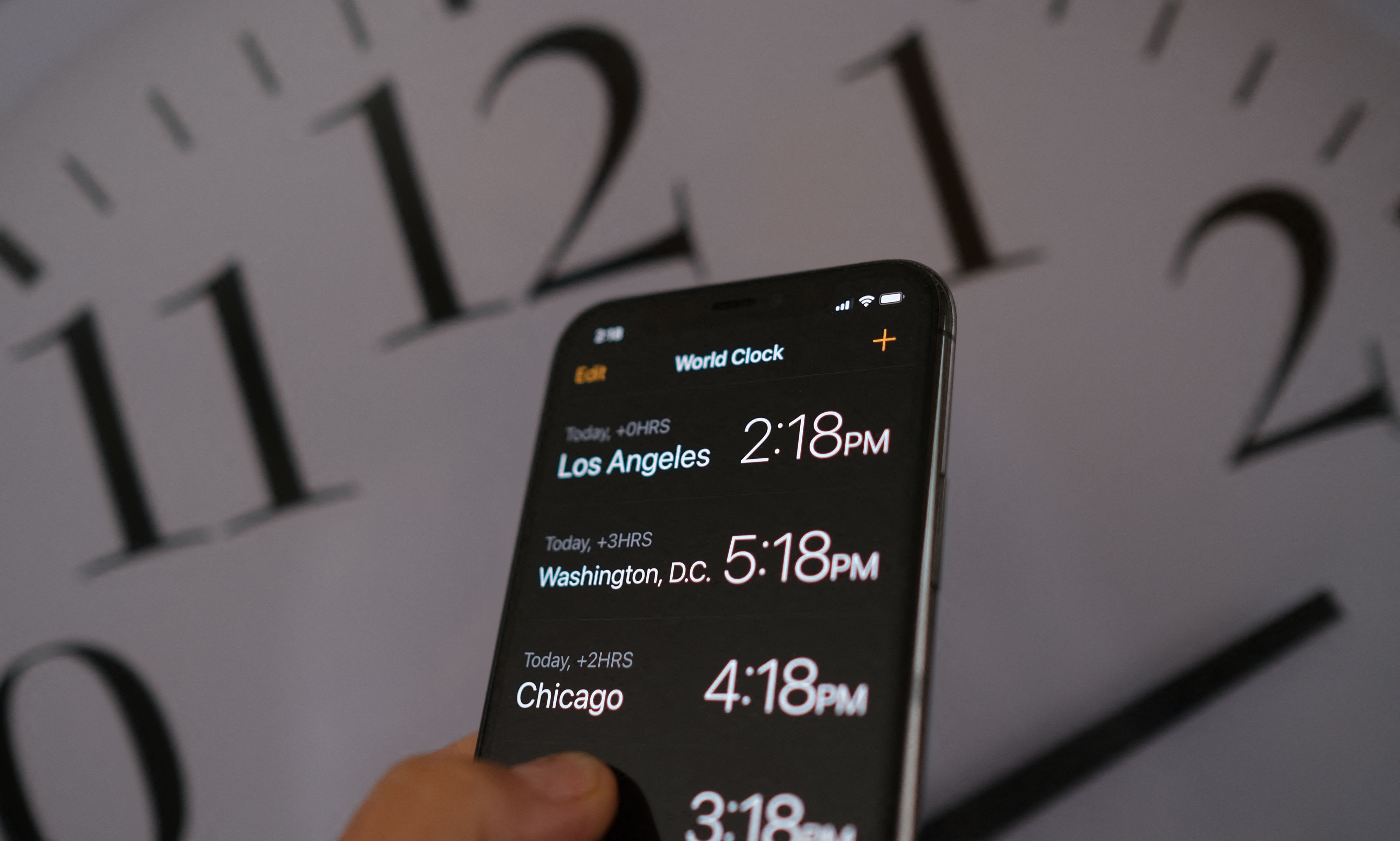 This illustration photo shows a clock in the background of a smartphone showing the time after daylight saving time was implemented in Los Angeles, California, on March 15, 2022.
