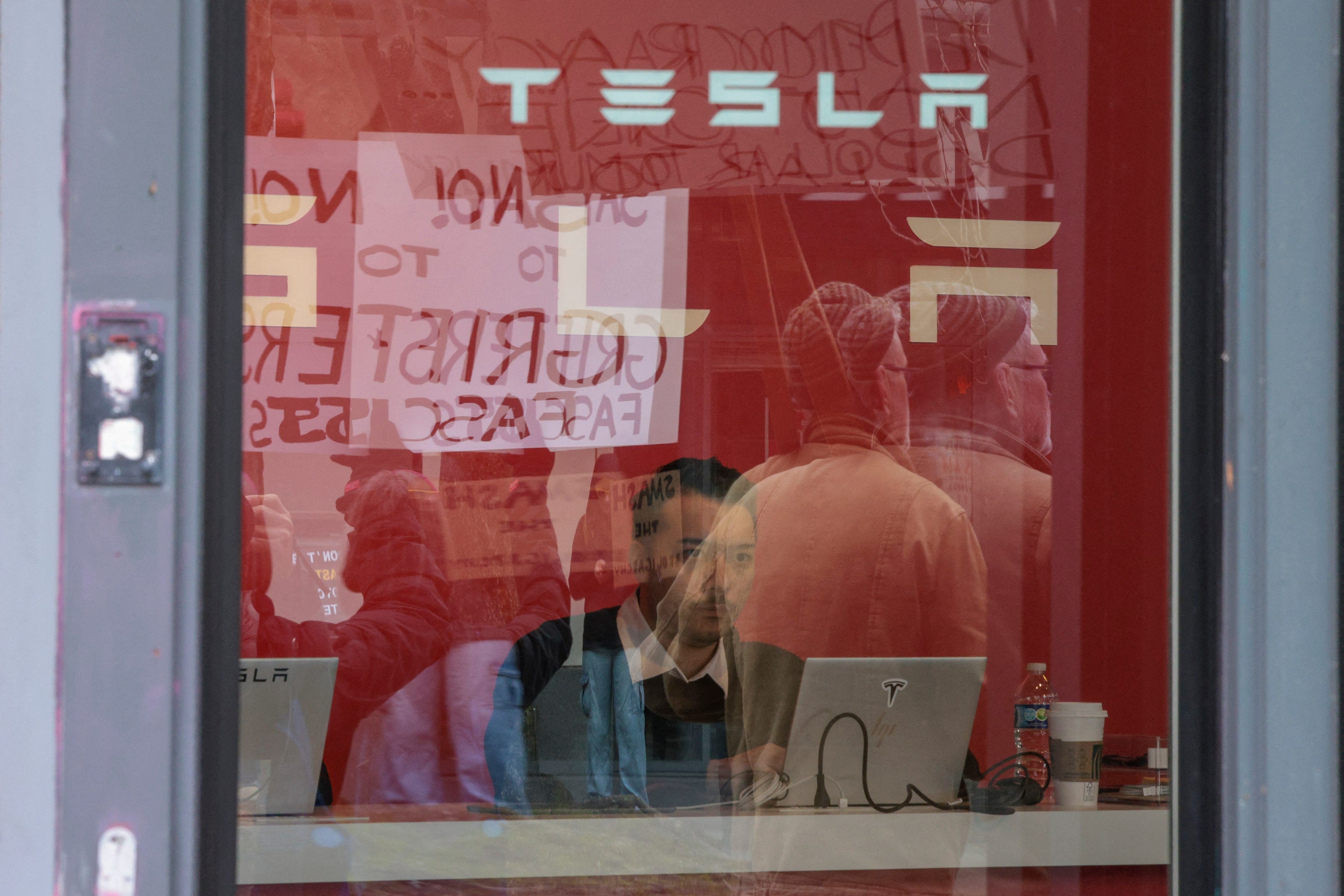 A Tesla employee looks on as people participate in a "TeslaTakedown" protest against Elon Musk outside of a Tesla showroom in Seattle, Washington, on Feb. 15, 2025. Musk leads the efforts under the newly created Department of Government Efficiency (DOGE), and was speaking at the White House with Trump, who has in recent weeks issued a flurry of orders aimed at slashing federal spending.