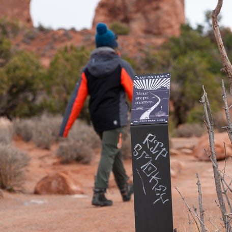 A visitor to Arches National Park walks past a park sign that has been vandalized to say "RIP Smokey," an apparent reference to federal budget cuts affecting public land management, on Monday, March 3, 2025.