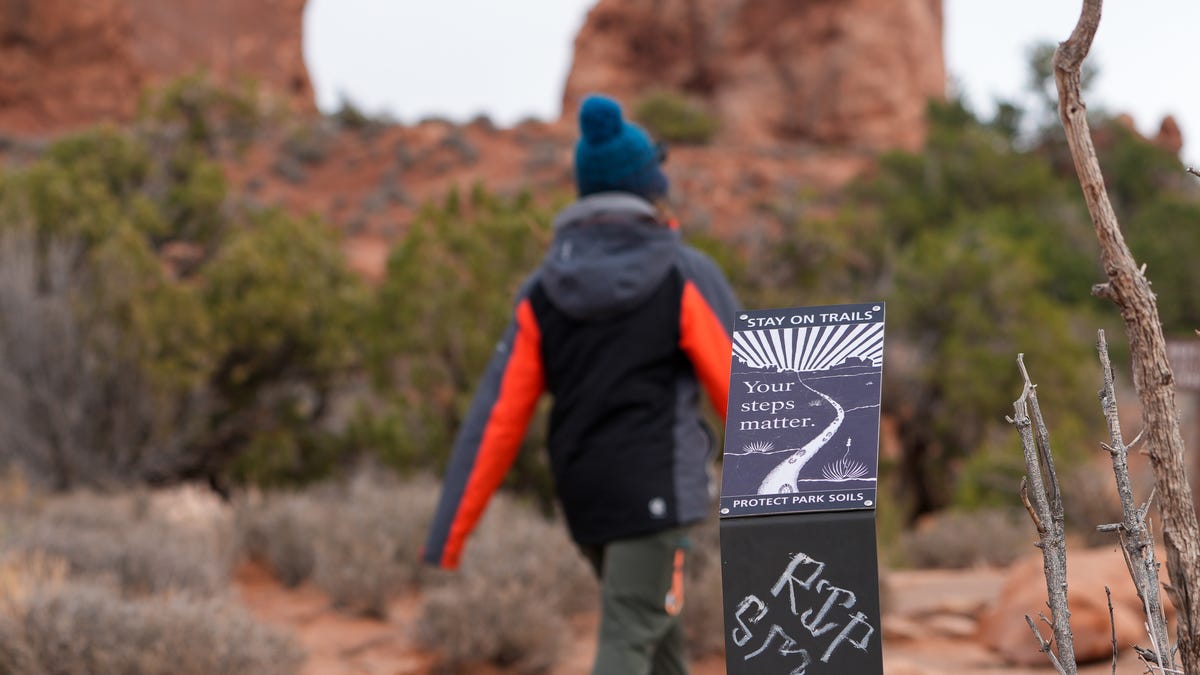 A visitor to Arches National Park walks past a park sign that has been vandalized to say "RIP Smokey," an apparent reference to federal budget cuts affecting public land management, on Monday, March 3, 2025.