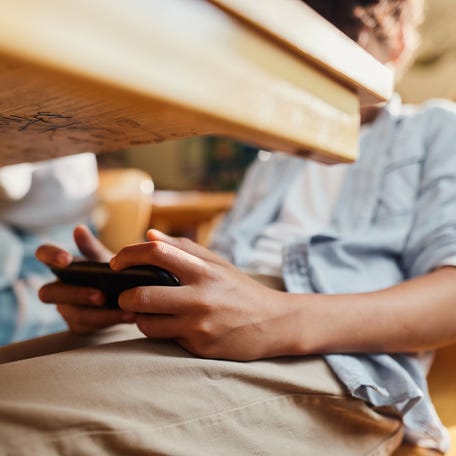 Close up of unrecognizable student using cell phone under the table during a class at elementary school.