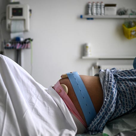 A pregnant woman lies on her bed with monitoring devices placed on her belly as she gets ready before delivering her child at the maternity ward of a hospital in Paris on June 29, 2022.