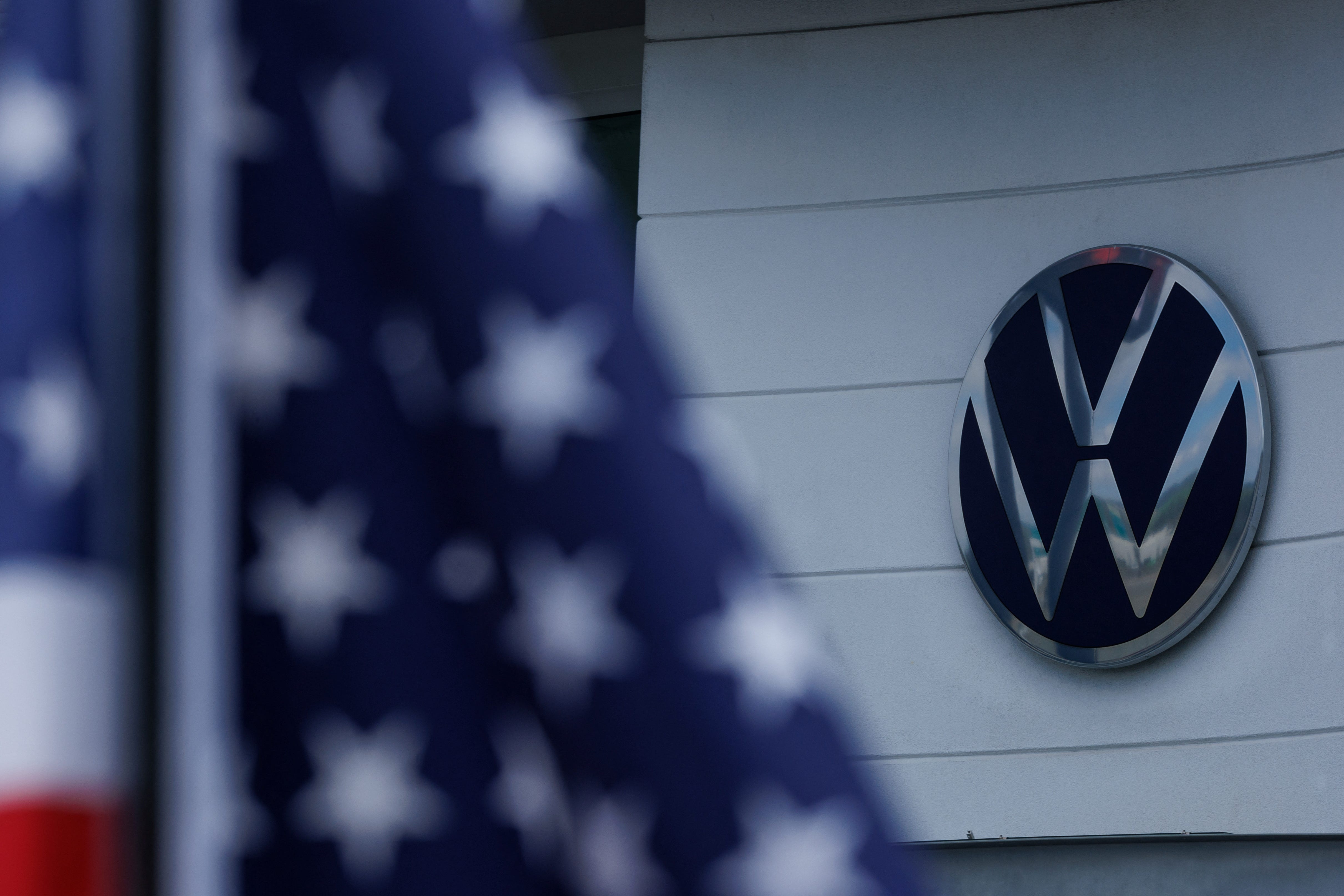 The Volkswagen logo is shown next to an American flag at a Volkswagen dealership in Irvine, California, U.S., March 27, 2025.