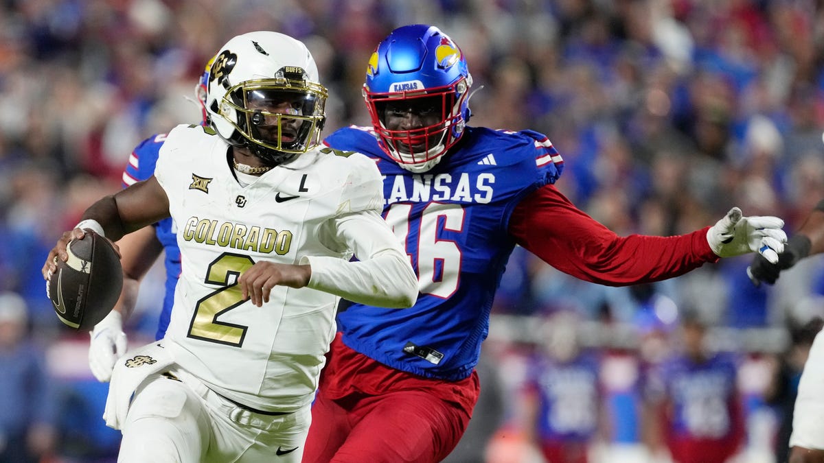 Quarterback Shedeur Sanders #2 of the Colorado Buffaloes is chased by defensive end Bai Jobe #46 of the Kansas Jayhawks as Sanders looks to pass in the second half at Arrowhead Stadium on November 23, 2024 in Kansas City, Missouri.