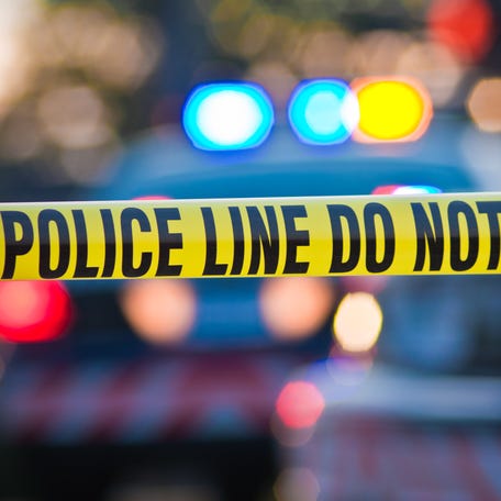 An image of a yellow law enforcement line with police car lights in the background.