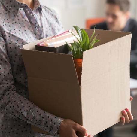 Employee holding cardboard box with belongings in company office.