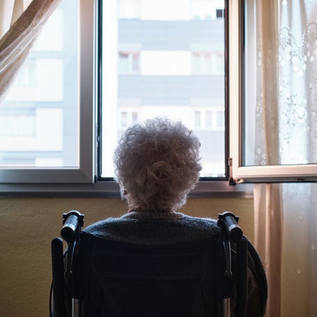 Rear view of an elderly woman sitting on wheelchair looking out the window at home.