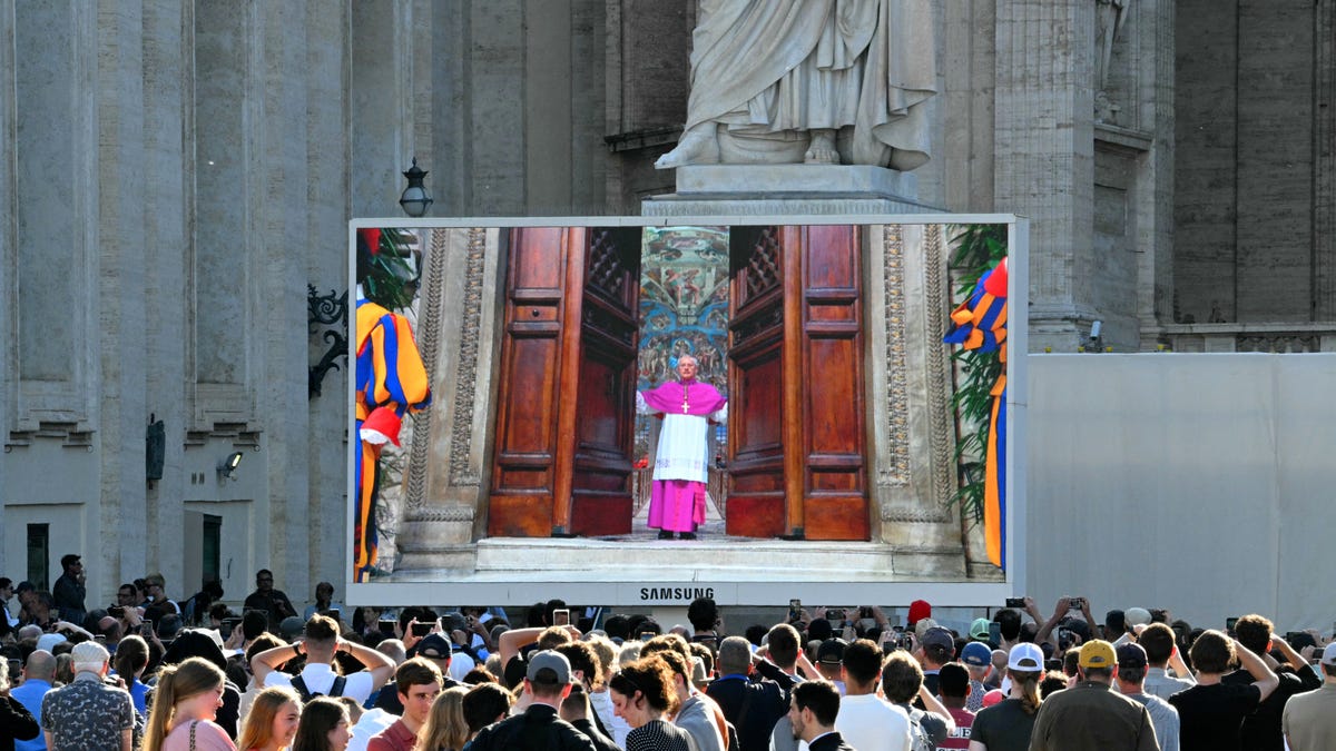 Faithful watch a giant screen displaying images of Diego Giovanni Ravelli, Master of Pontifical Liturgical Celebrations, closing the doors of the Sistine chapel as the conclave to elect a new Pope starts, at St Peter's Square in The Vatican, on May 7, 2025.