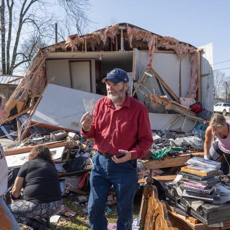 Tim Striegel goes though his damaged belongings and finds a single unbroken drinking glass, while volunteers help him clean up the morning after his mobile home was hit by a tornado on March 16, 2025 in Calera, Alabama.