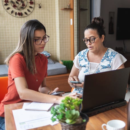 Mother and daughter doing finances together at home. T